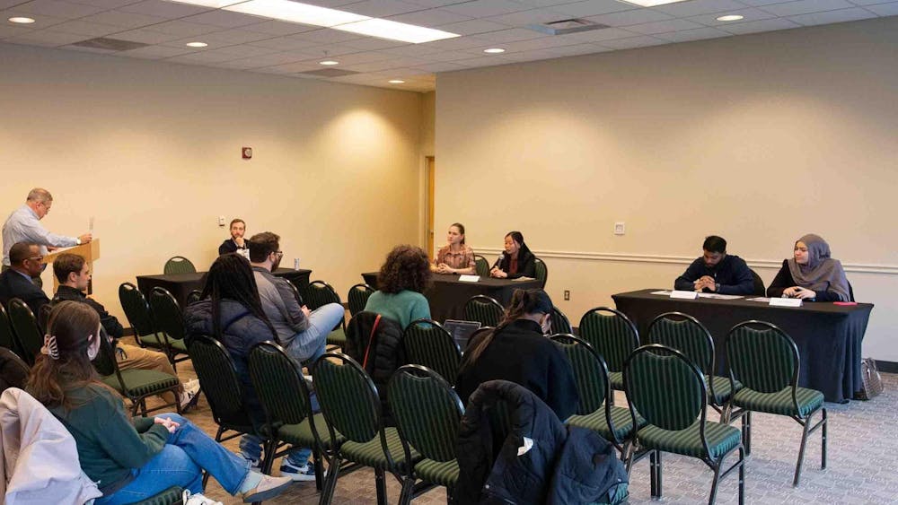 At two tables, candidates from each presidential ticket sit and answer questions. Attendees watch from rows of chairs.