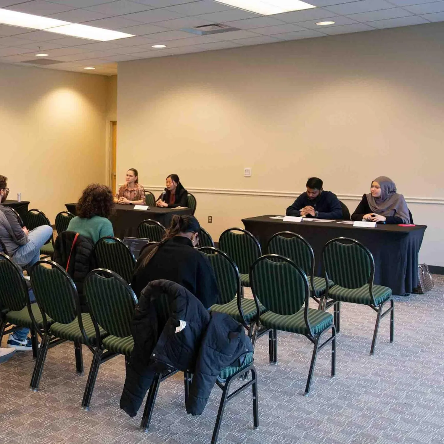 At two tables, candidates from each presidential ticket sit and answer questions. Attendees watch from rows of chairs.