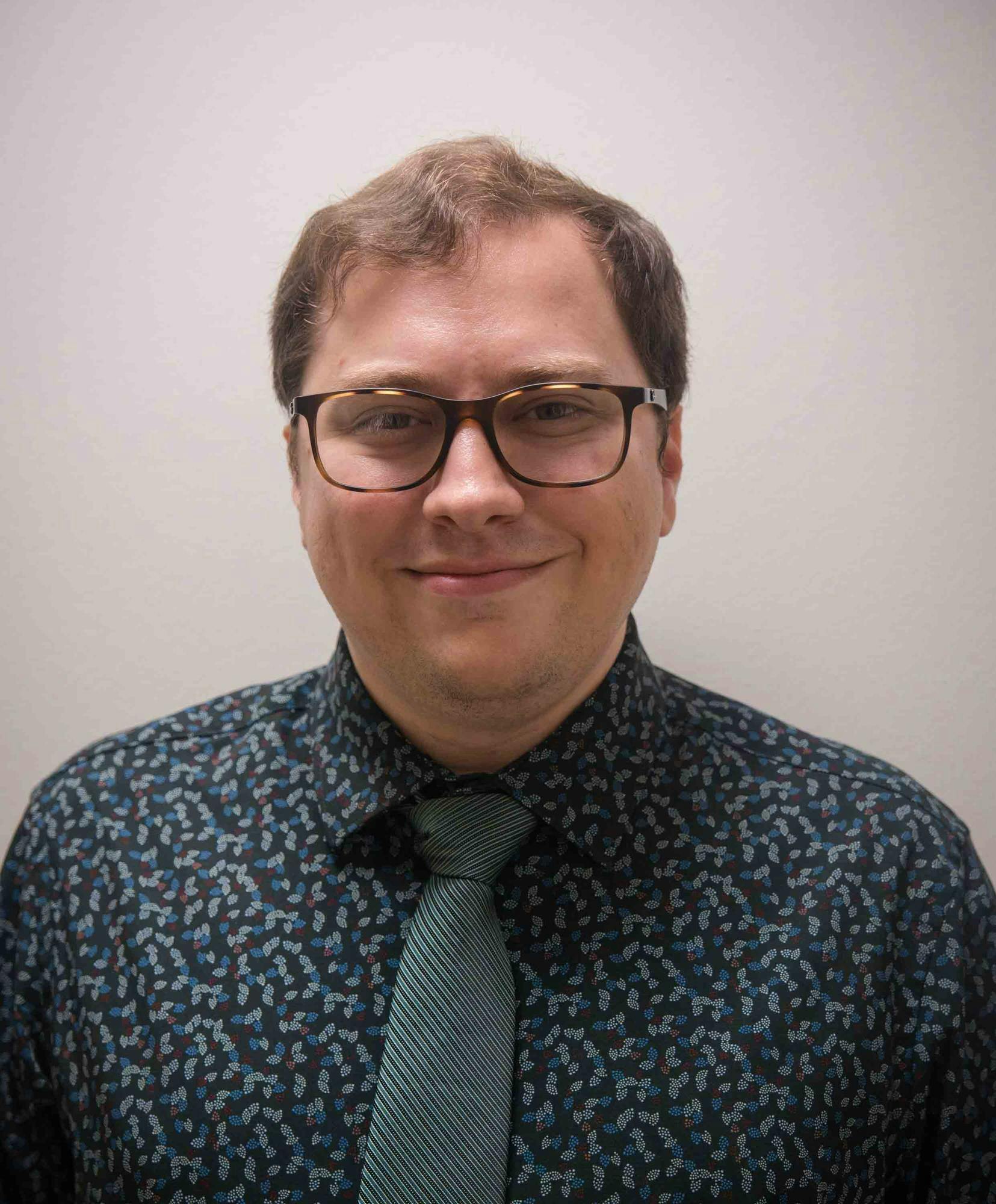 A man with brown hair and glasses smiles.