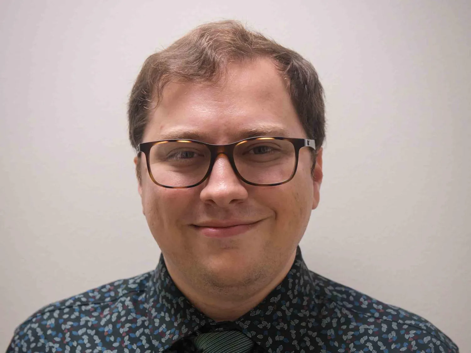 A man with brown hair and glasses smiles.