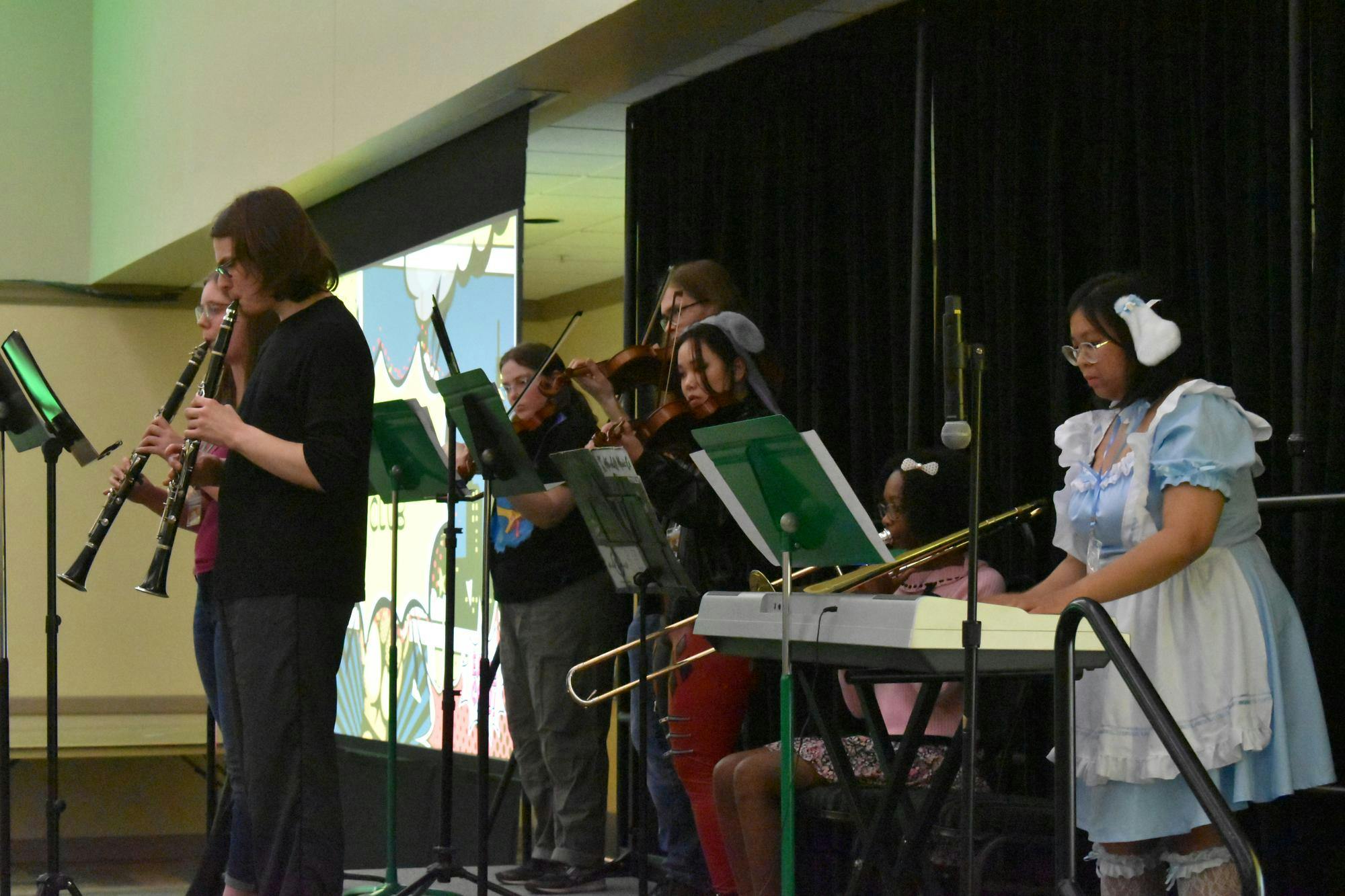7 people play instruments on stage, including clarinet, piano, trombone, and violin.