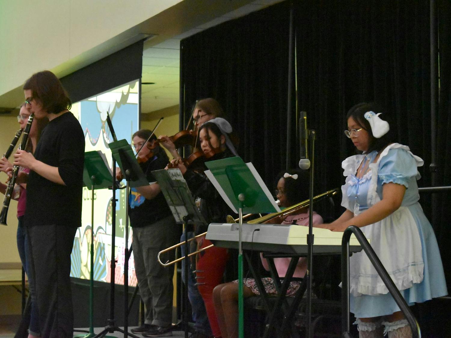 7 people play instruments on stage, including clarinet, piano, trombone, and violin.