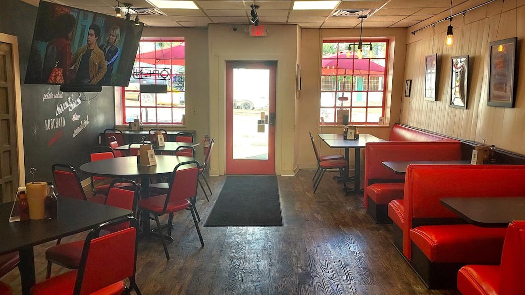 The restaurant indoors is a dining area with black tables, red chairs, and red couches. A TV screen plays TV shows in the background.