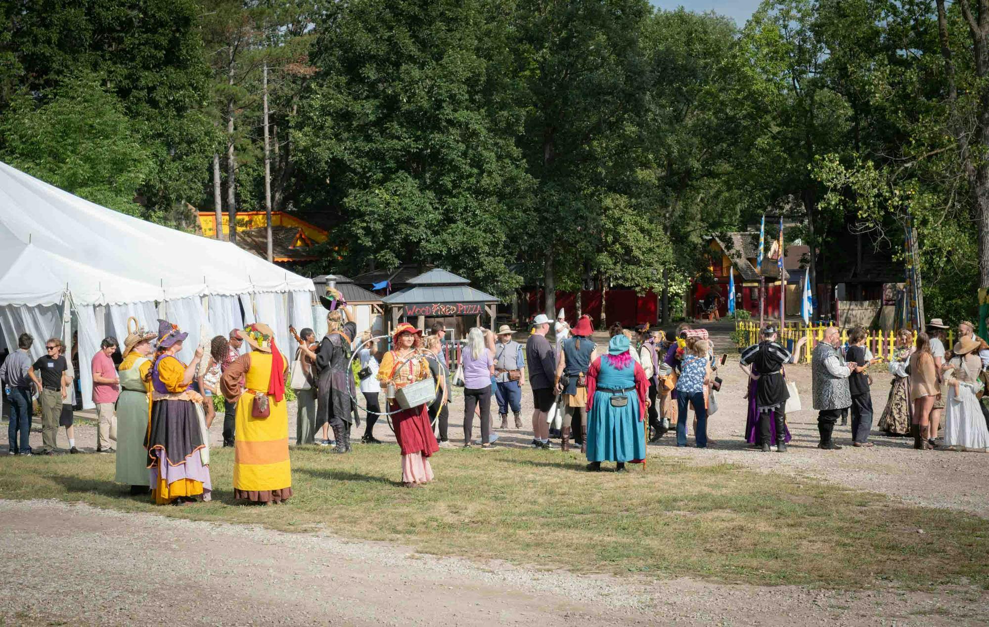 Attendees and cast members gather on festival grounds, many dressed in renaissance attire.