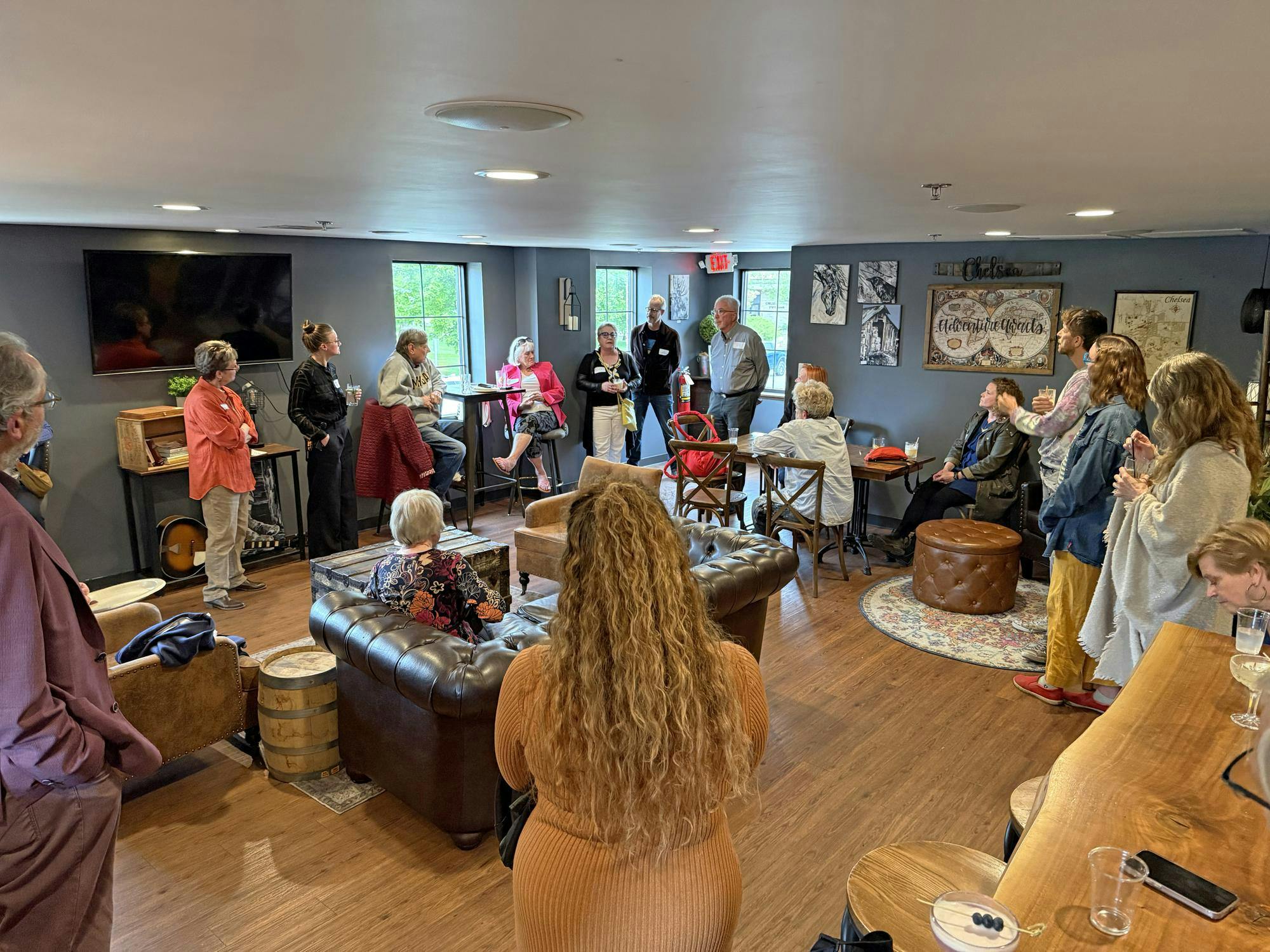 A group of people standing along the walls in a room talking to each other.