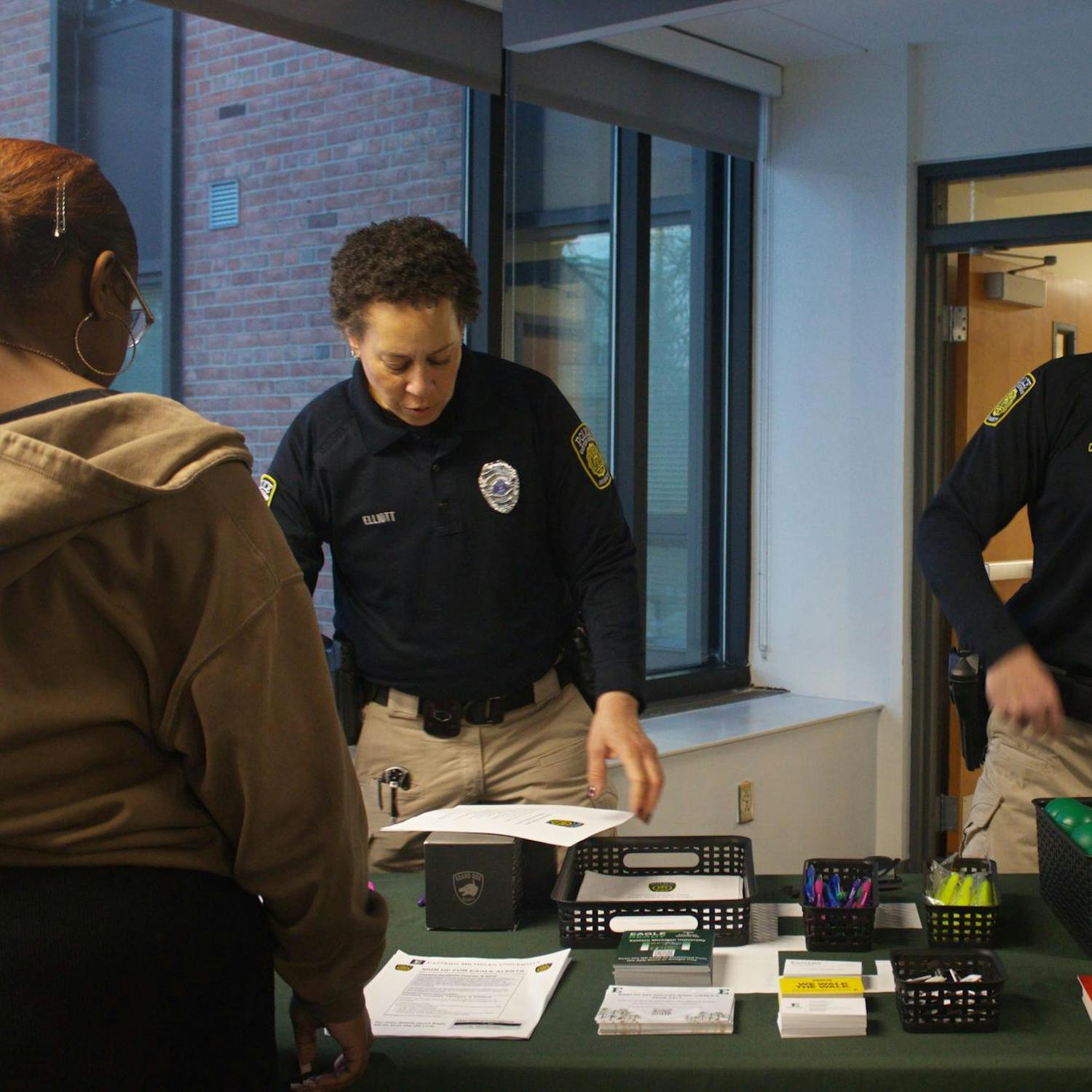 Two campus police officers in uniform talk to two Eastern Michigan students while standing behind an information table.
