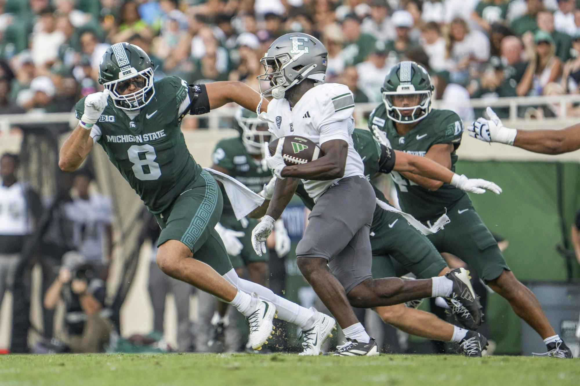 An EMU player holds the ball while MSU players rush towards him on the field.