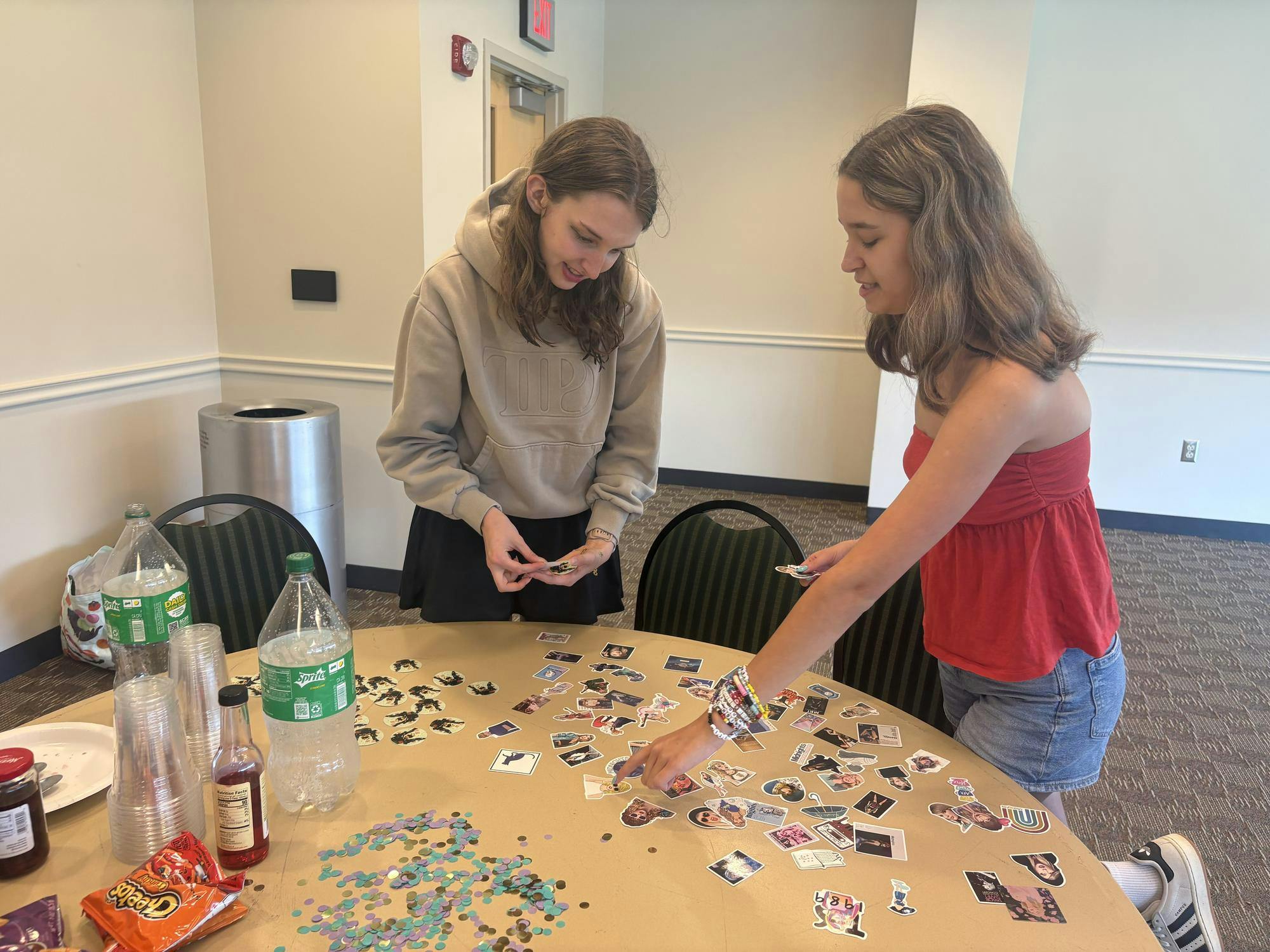 Two students stand at a table covered with Taylor Swift-themed stickers and choose their favorites.