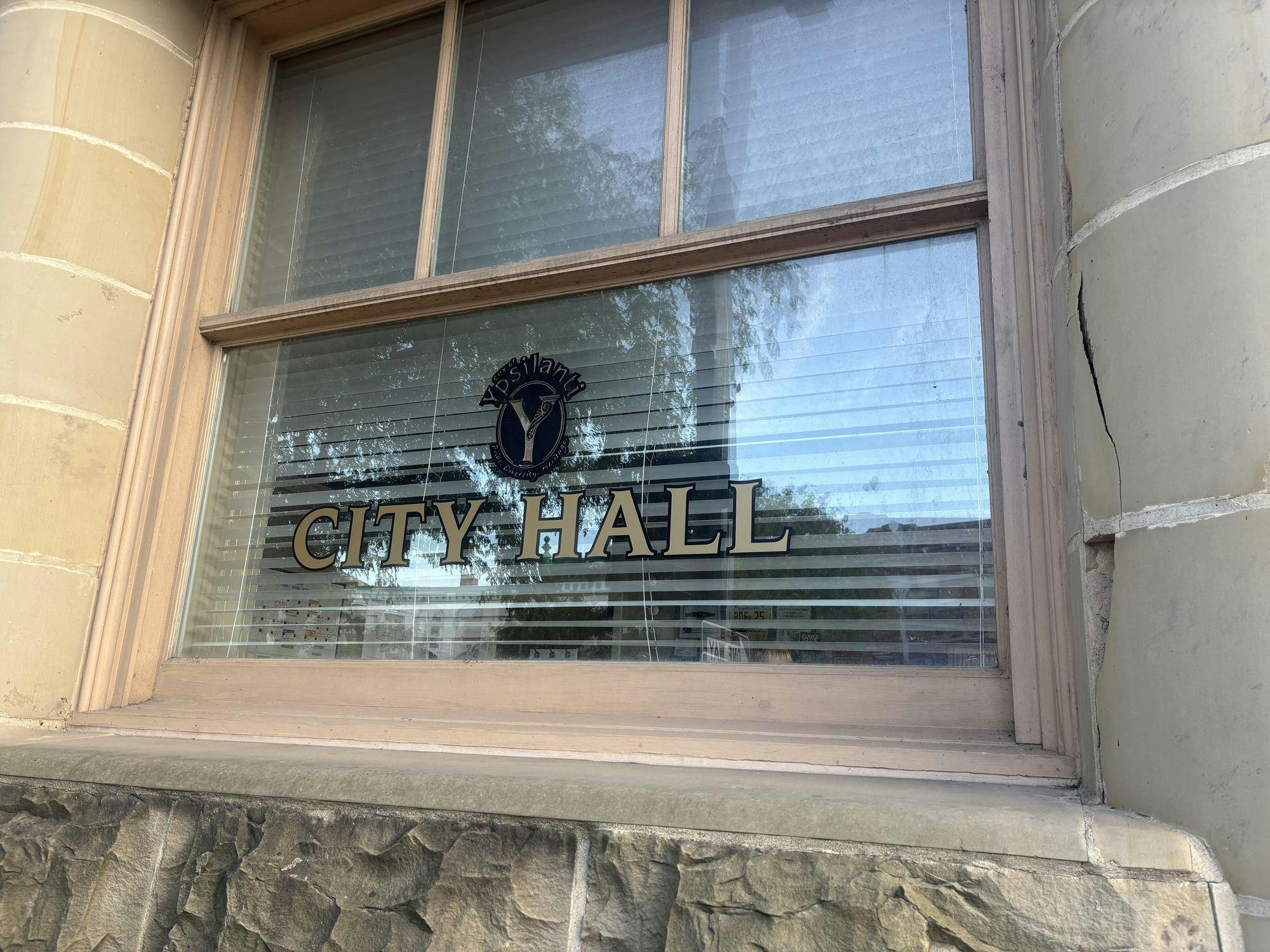 A close-up of a brick building with columns shows the words, "City Hall" painted on the window.