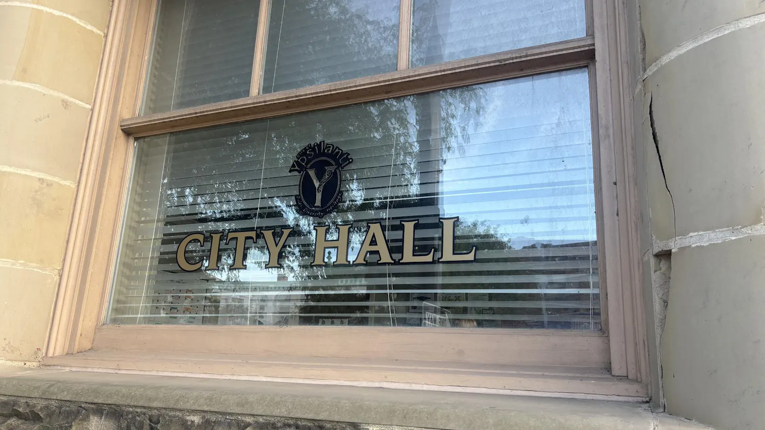 A close-up of a brick building with columns shows the words, "City Hall" painted on the window.