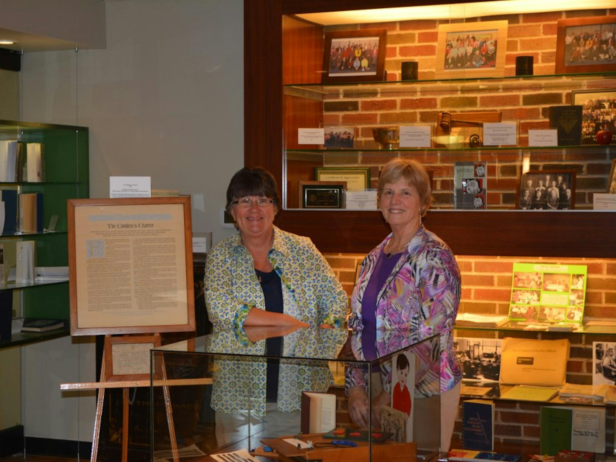 	Lynne Rocklage (left) and Nancy Halmhuber Navarre (right) standing in front of the School of Education display in the McKenny Hall Art Gallery.