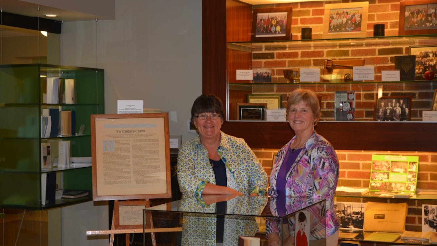 	Lynne Rocklage (left) and Nancy Halmhuber Navarre (right) standing in front of the School of Education display in the McKenny Hall Art Gallery.
