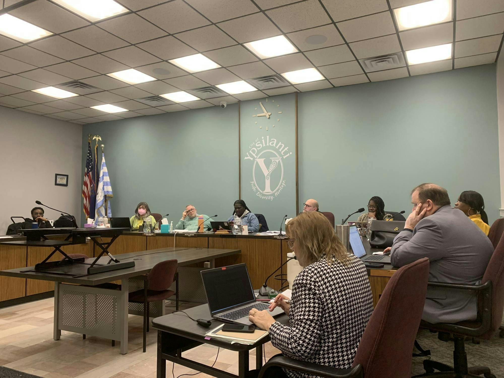 9 members of City Council staff sit around a table inside City Hall while listening to public commentators.