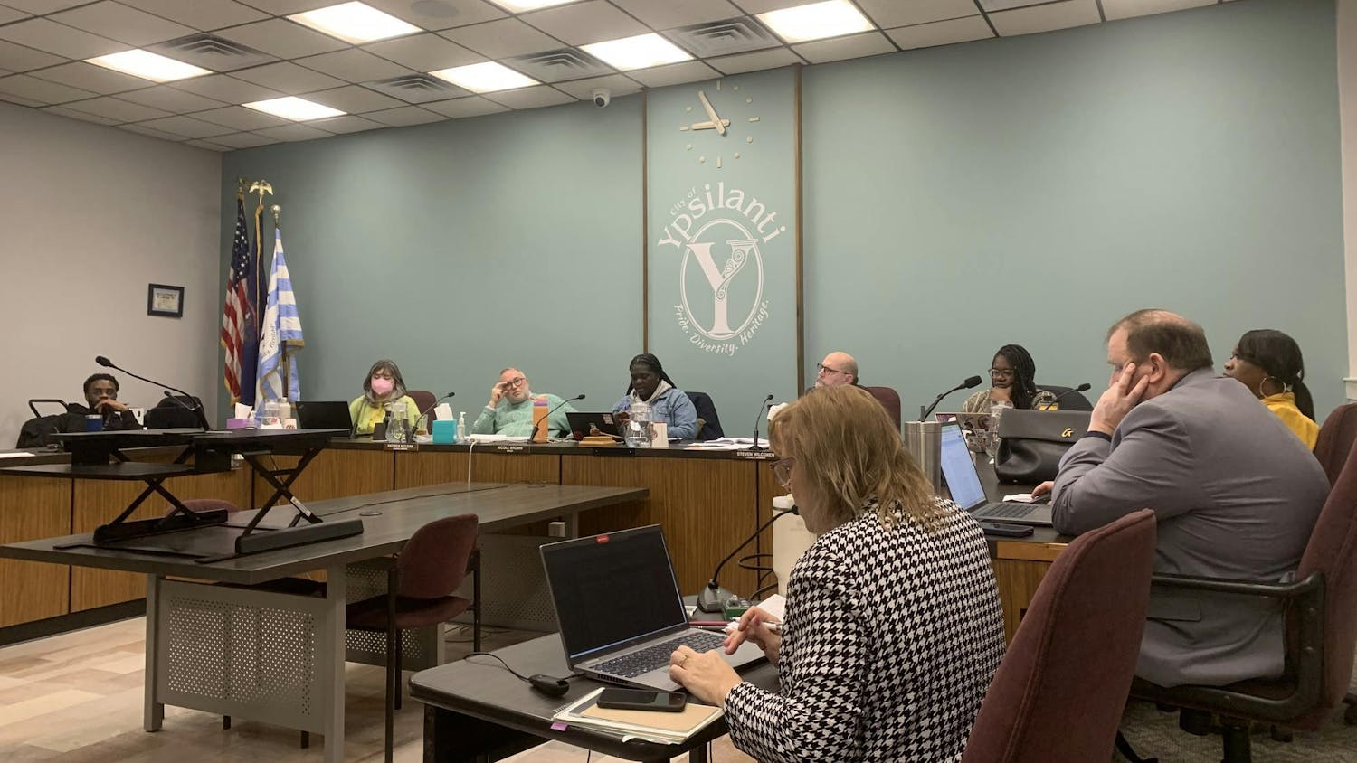 9 members of City Council staff sit around a table inside City Hall while listening to public commentators.