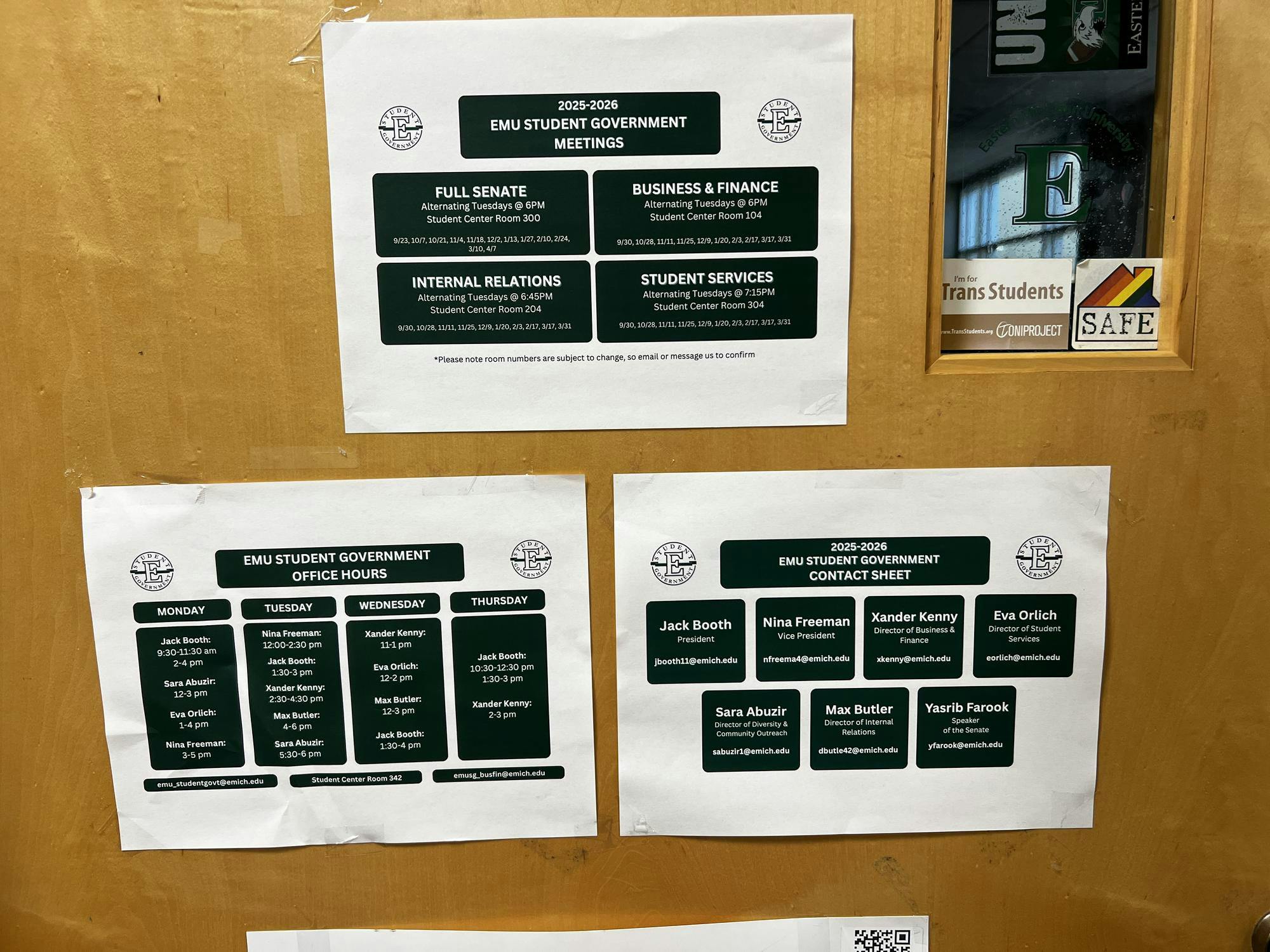 Three signs on the door of the student government office. One is for the times and locations of meetings for the semester. The second one has the office hours of various student government members. The third one is a contact sheet for the president, vice president, the directors of the committees, and the speaker of the senate.