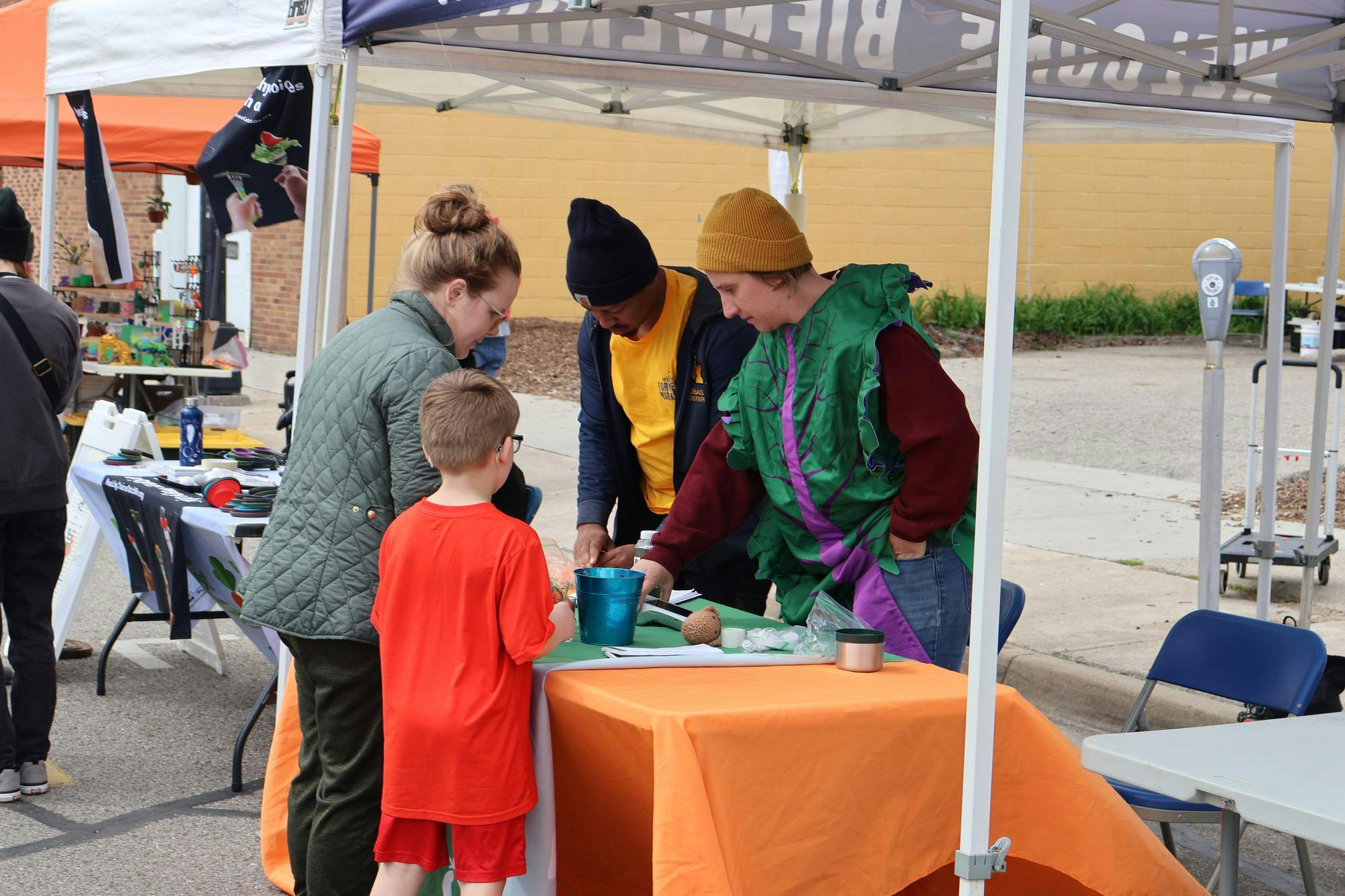 An adult and child stop by a stand at the farmer's market and talk to two staff members.