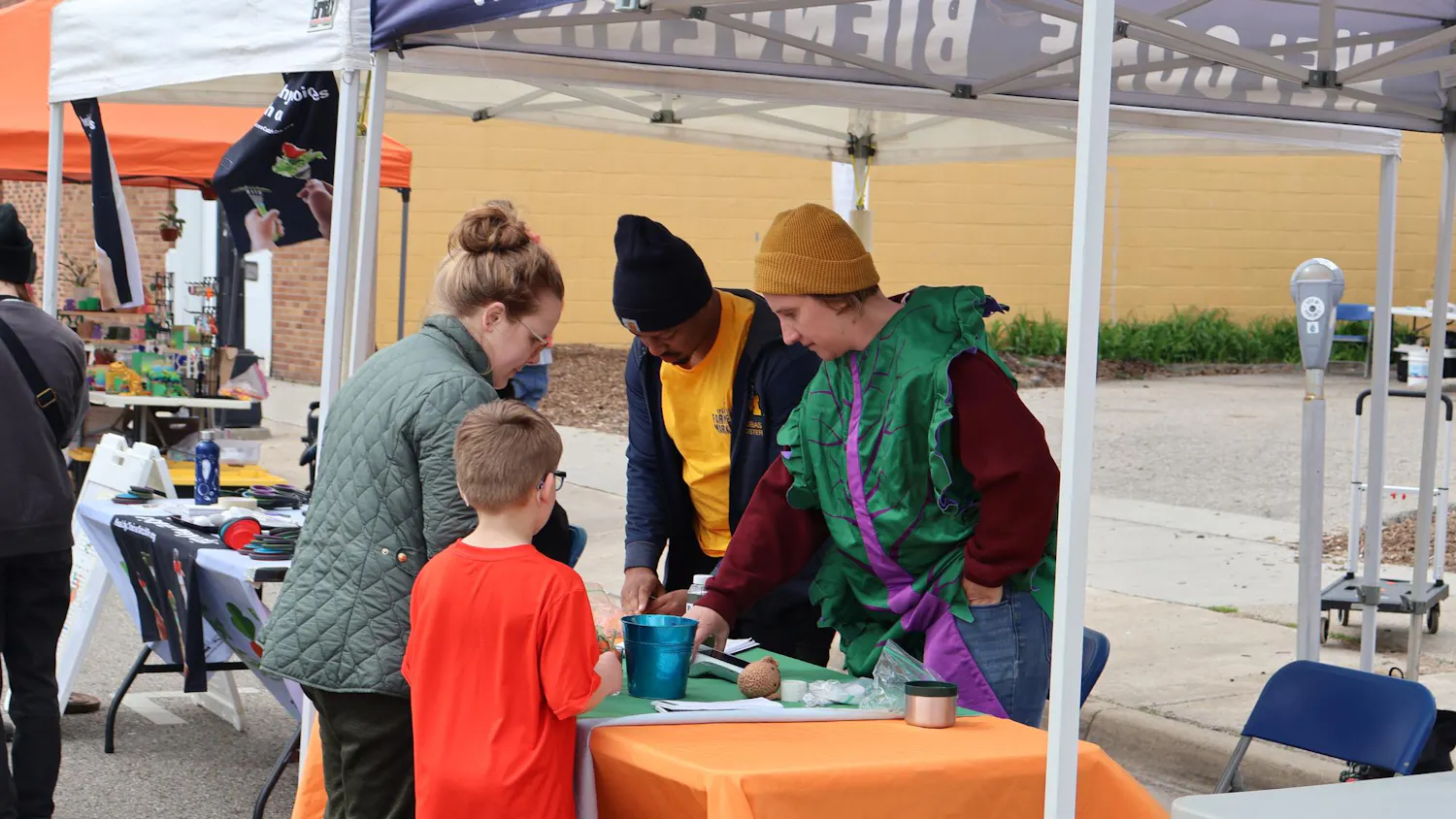 An adult and child stop by a stand at the farmer's market and talk to two staff members.