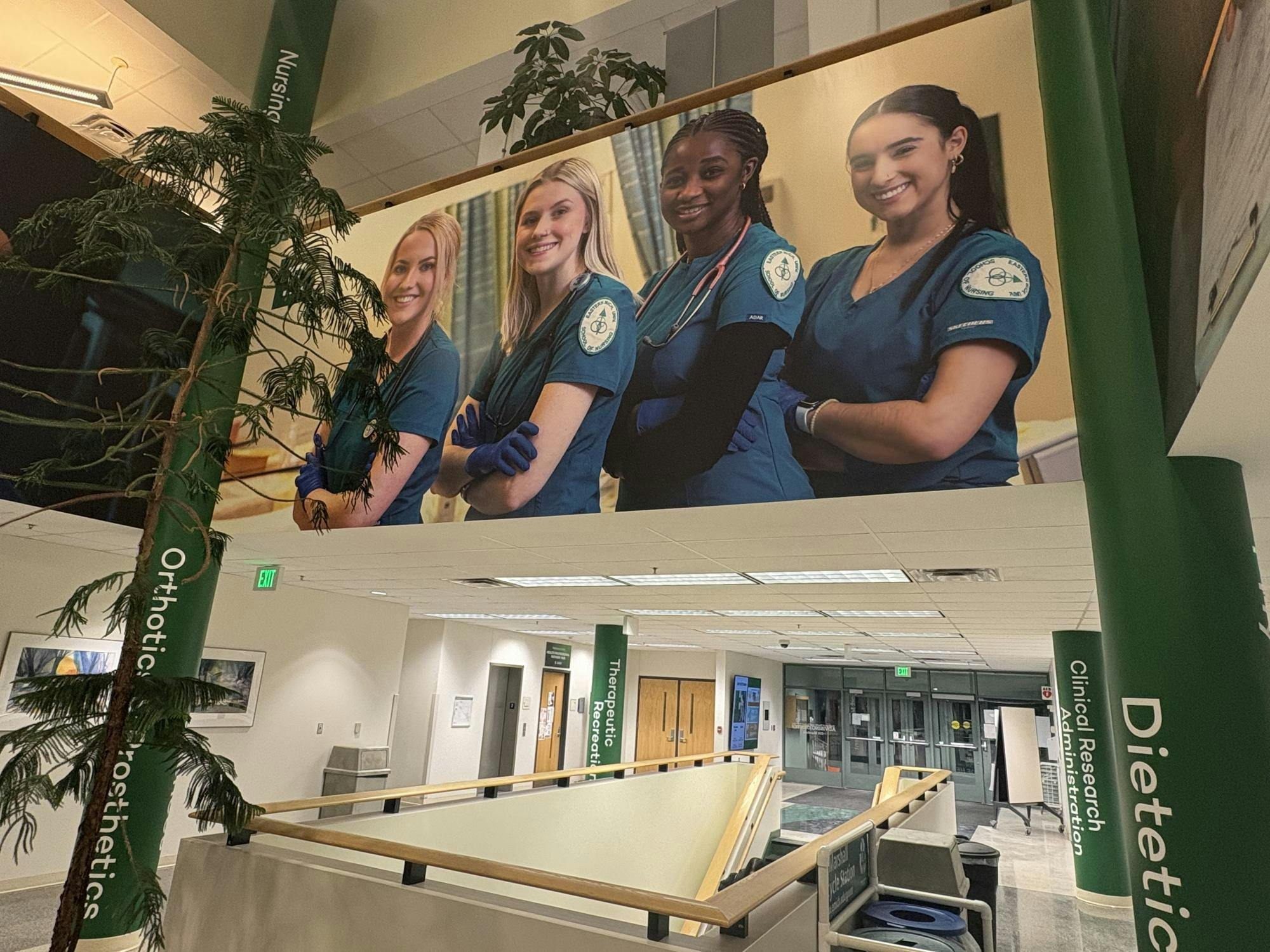 Green pillars with the words &quot;nursing,&quot; &quot;clinical research administration&quot; and &quot;dietician&quot; frame a large photo of nursing students displayed in the Everett Marshall Health and Human Services building. 