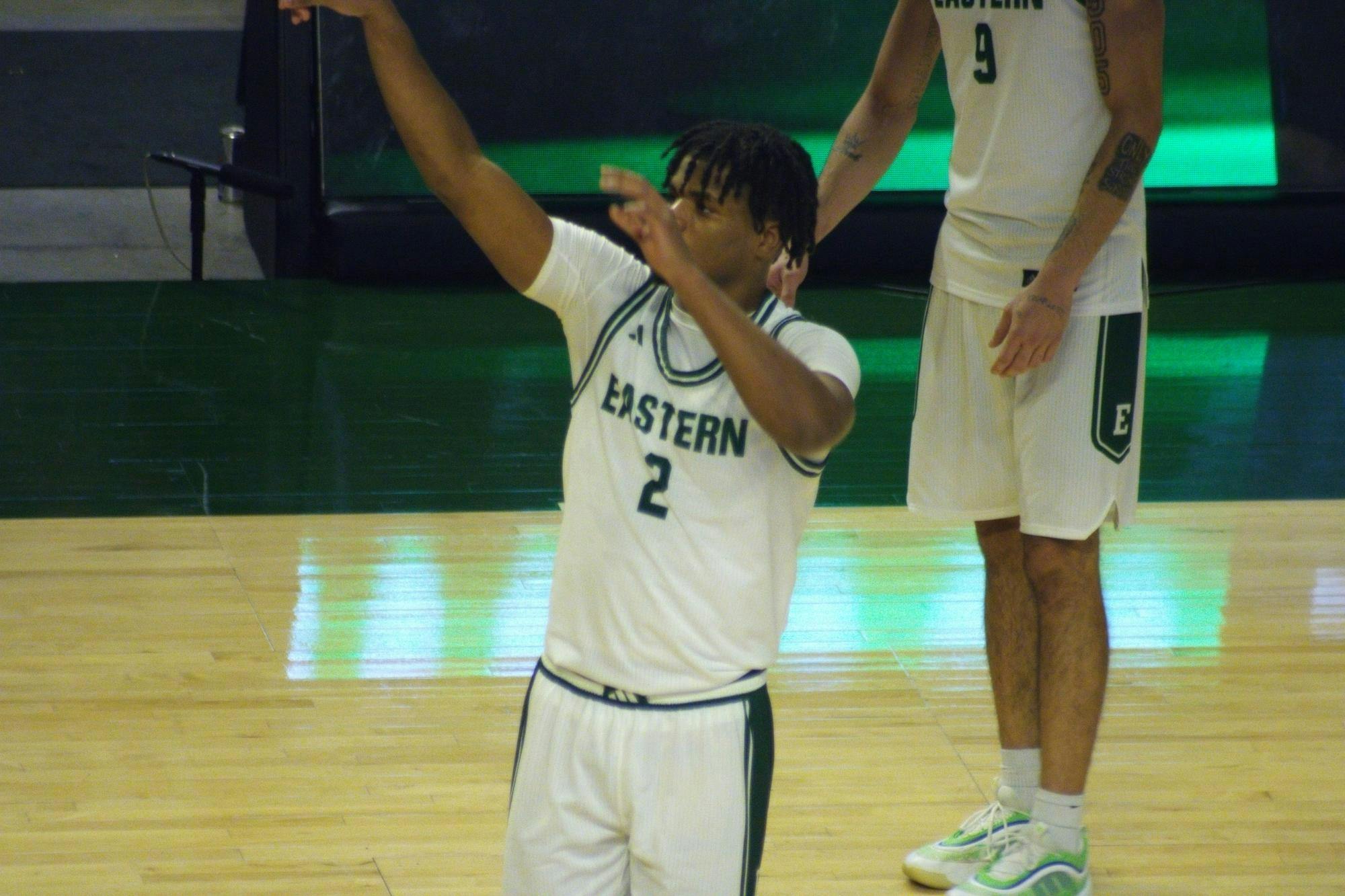 Carlos Hart, EMU player #2, stands in a green and white jersey on the court with his hands raised.
