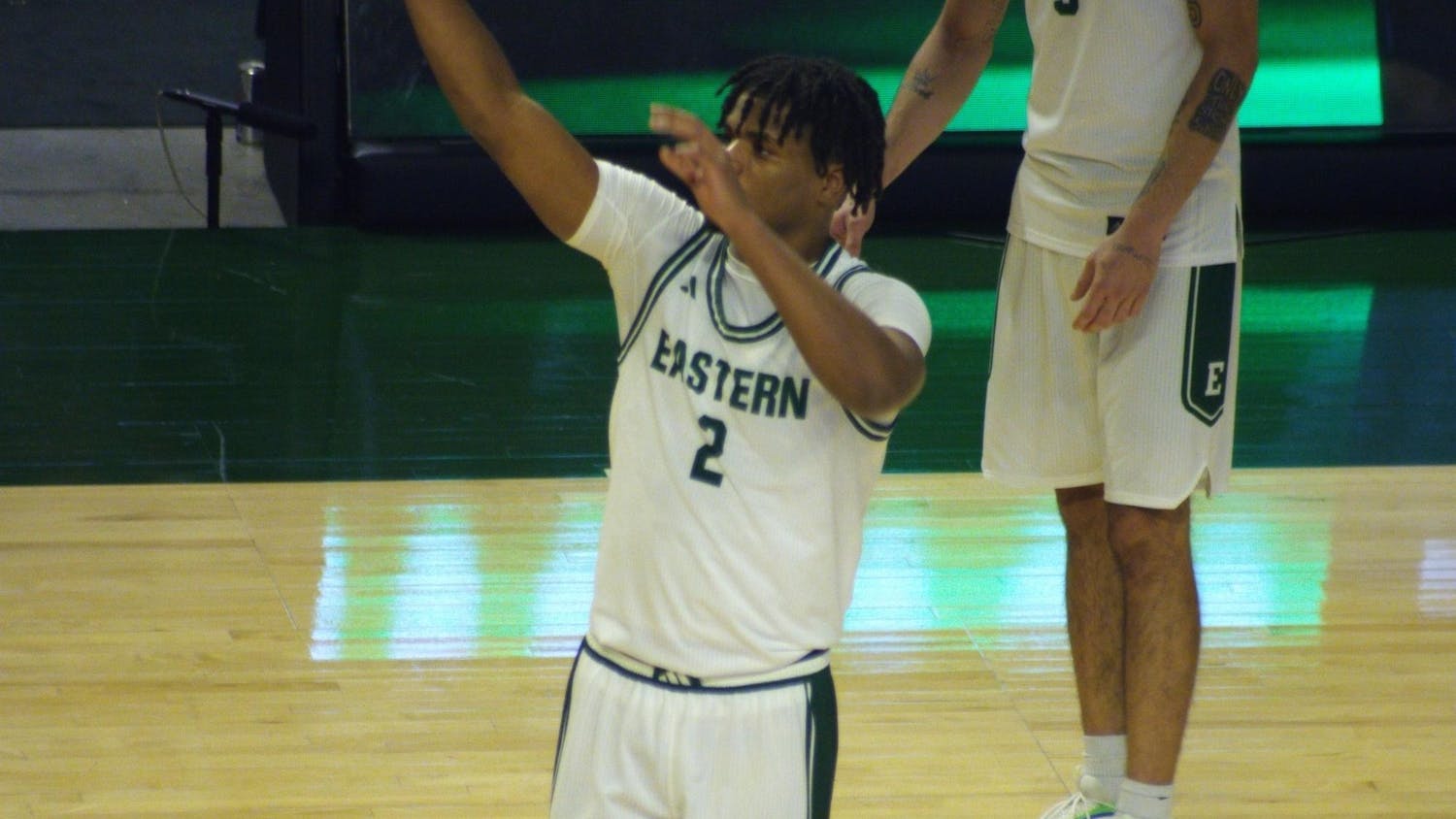 Carlos Hart, EMU player #2, stands in a green and white jersey on the court with his hands raised.