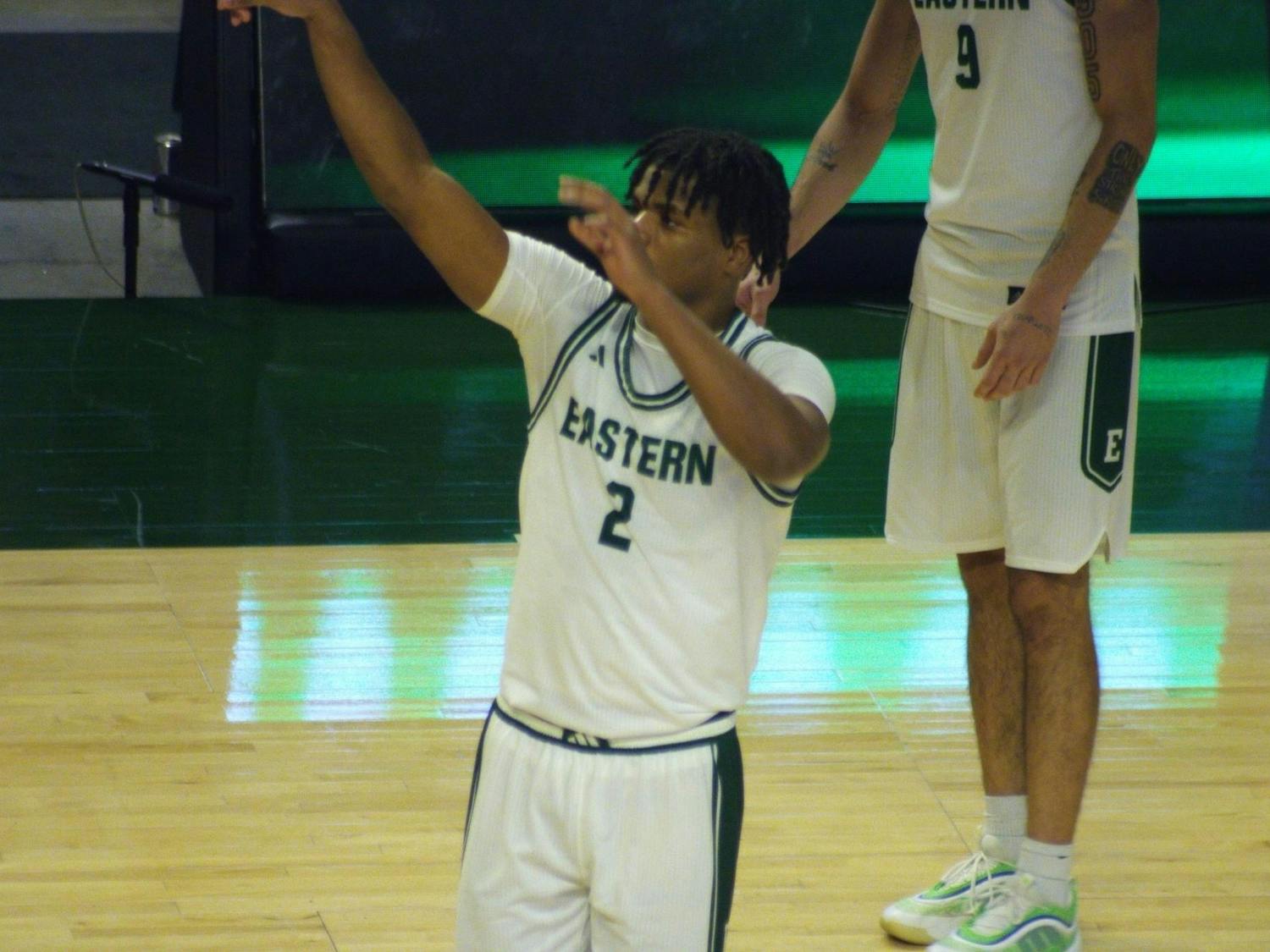 Carlos Hart, EMU player #2, stands in a green and white jersey on the court with his hands raised.