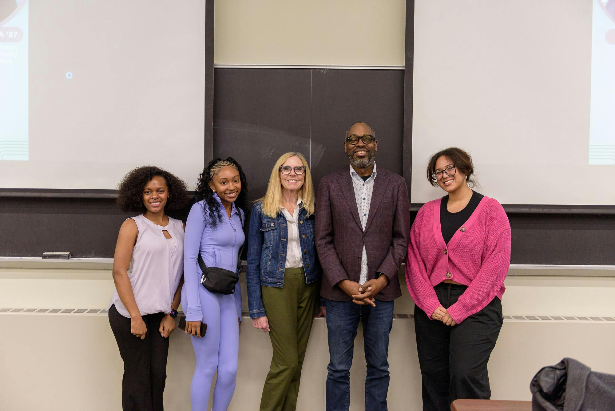 A group photo of 5 people in front of a blackboard and 2 projector screens.