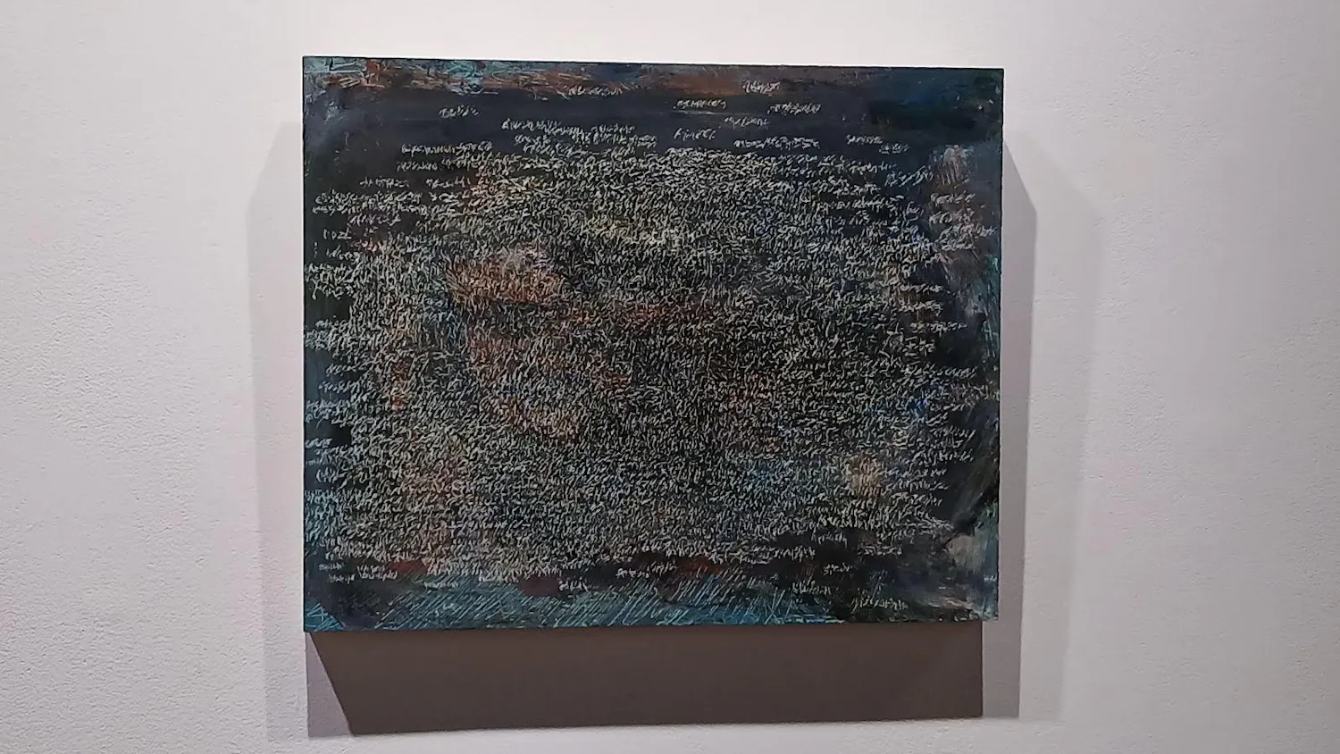 An abstract painting of scratches on a blue background hanging on a white wall.