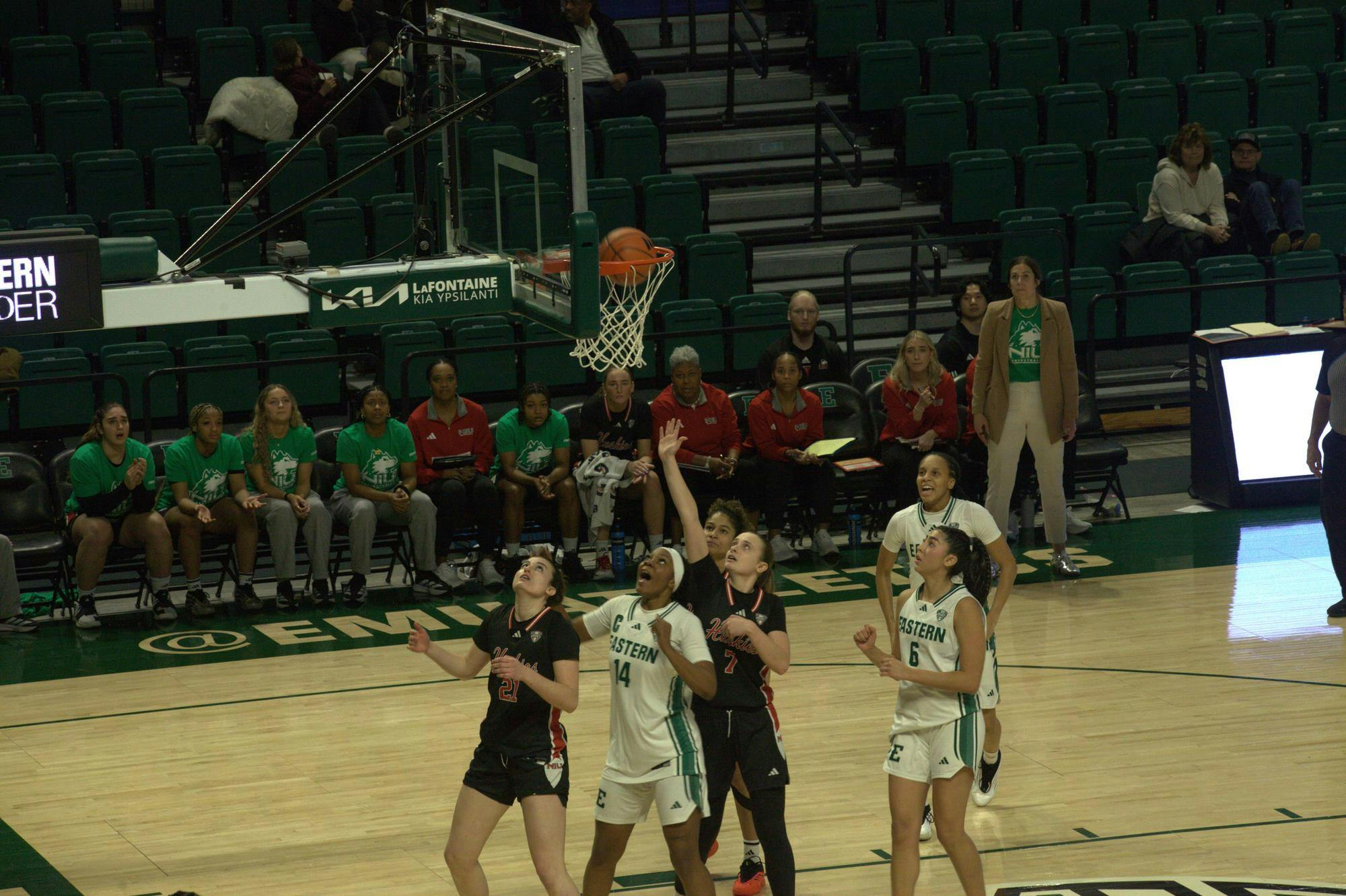 Eastern Michigan Women's basketball players celebrate successful shot as ball goes into the hoop.