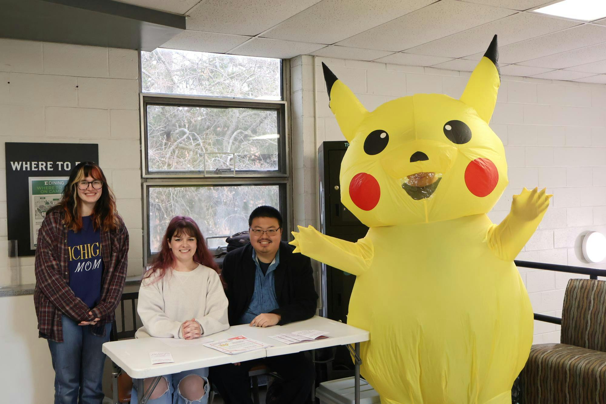 Three people at a table next to a Pikachu mascot.