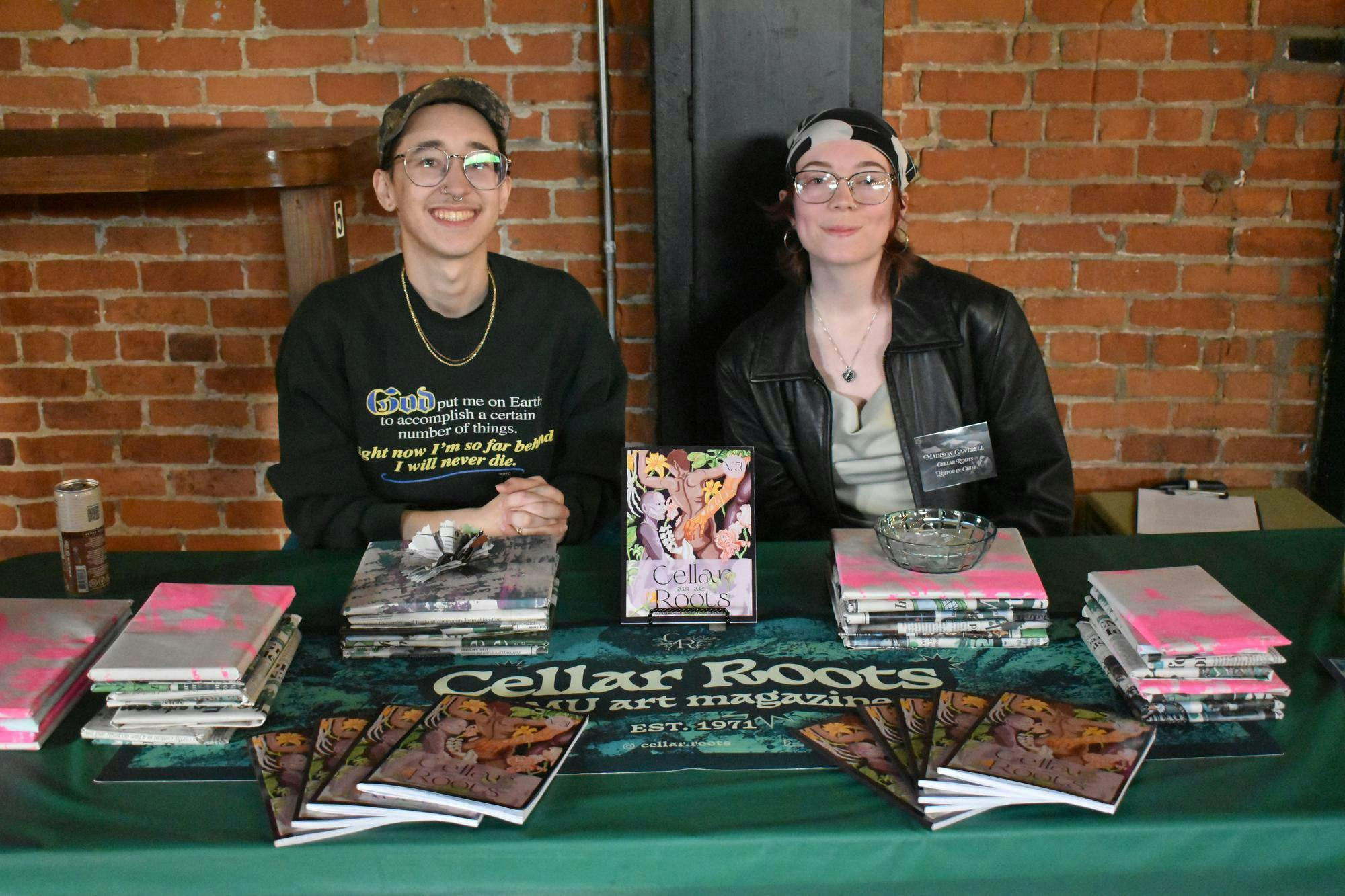 Laurence Bourdeau and Madison Cantrell sit at a table full of Cellar Roots magazines.