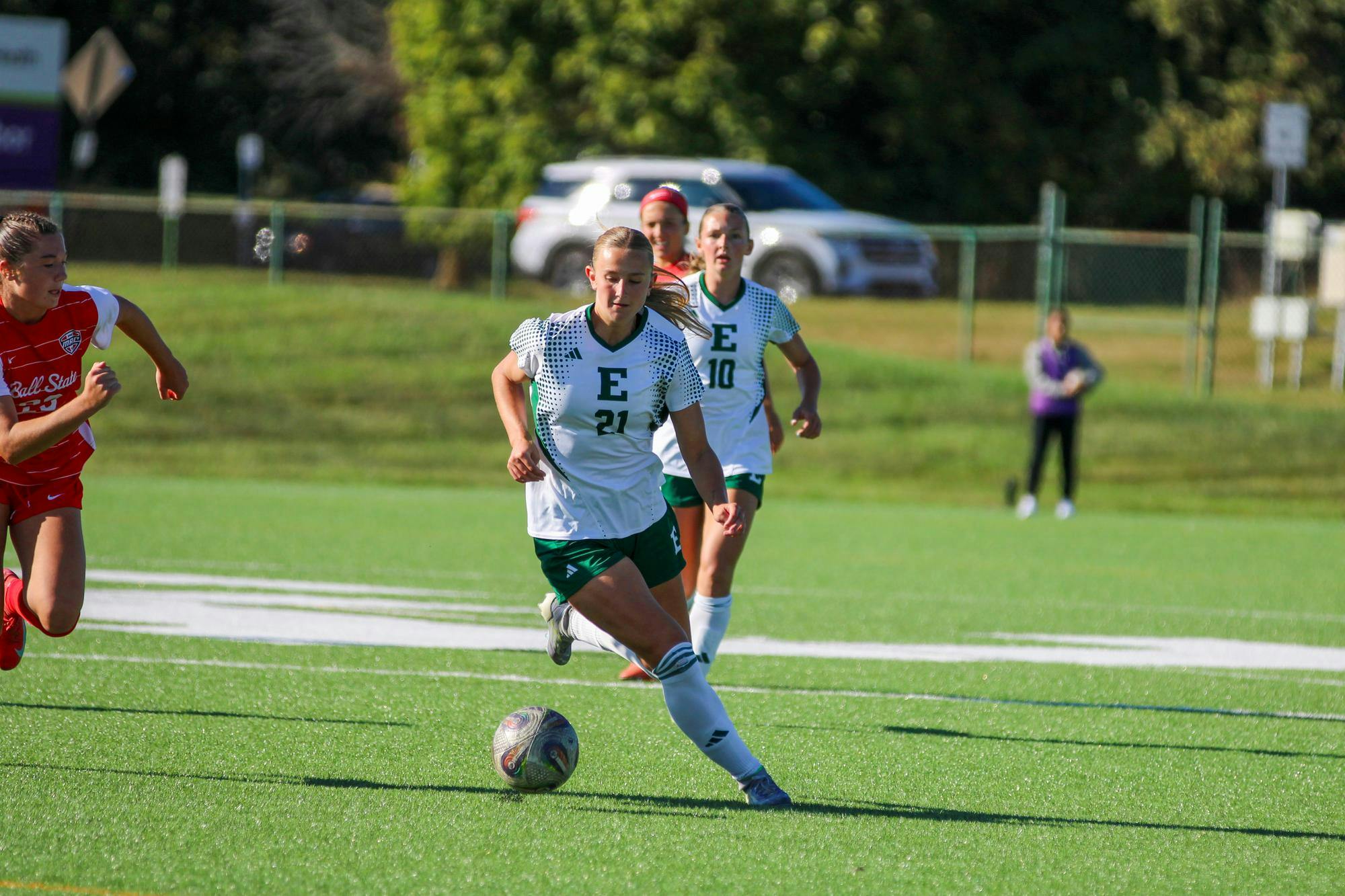 EMU&#039;s player, in a white jersey, dribbling the ball with a Ball State player, in a red jersey, coming in from the side