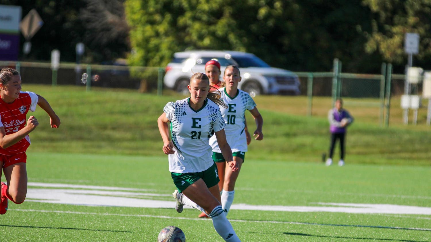 EMU's player, in a white jersey, dribbling the ball with a Ball State player, in a red jersey, coming in from the side