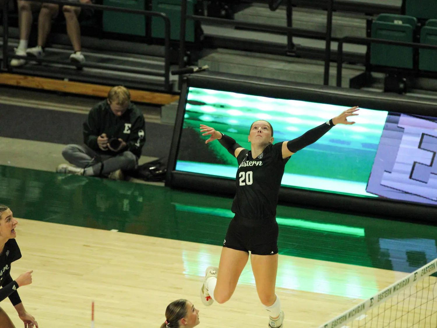 #20 AshleeKay Christensen, in a black jersey, preparing to spike the ball over the volleyball net.