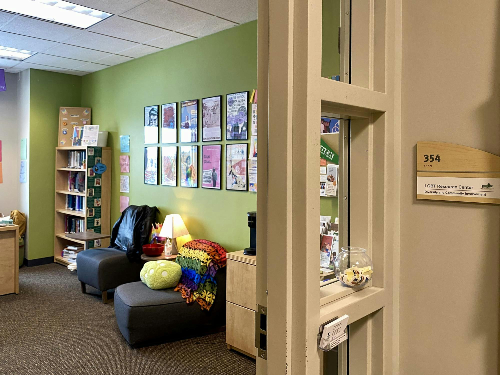 Colorful office room with cushioned seating and several posters on the wall. The photo is taken from outside the doorway looking in.