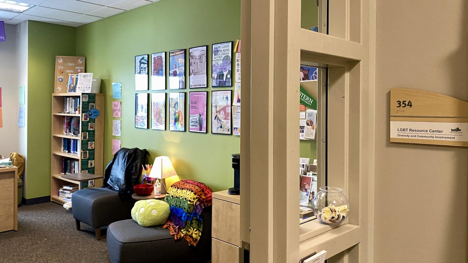Colorful office room with cushioned seating and several posters on the wall. The photo is taken from outside the doorway looking in.