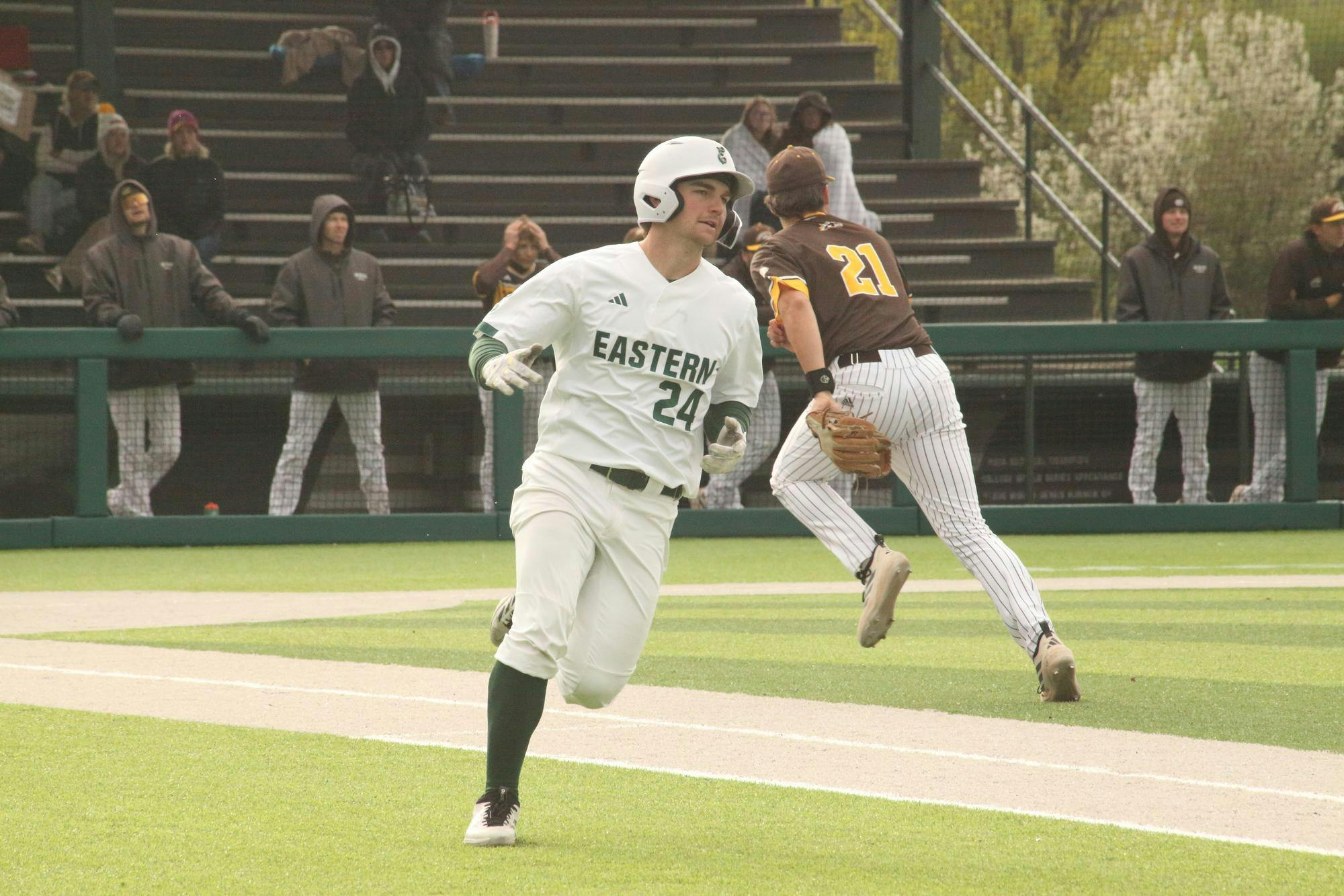 Baseball player runs from home to first base while a member of the opposing team runs in the opposite direction in the background.