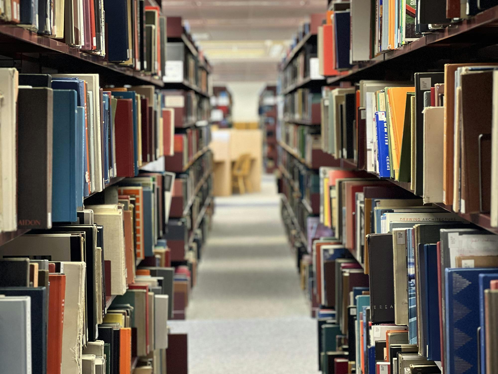 Books with covers in many different colors fill the shelves of a dark brown bookcase in the Eastern Michigan University Halle Library.