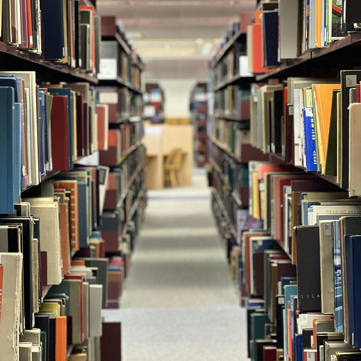 Books with covers in many different colors fill the shelves of a dark brown bookcase in the Eastern Michigan University Halle Library.