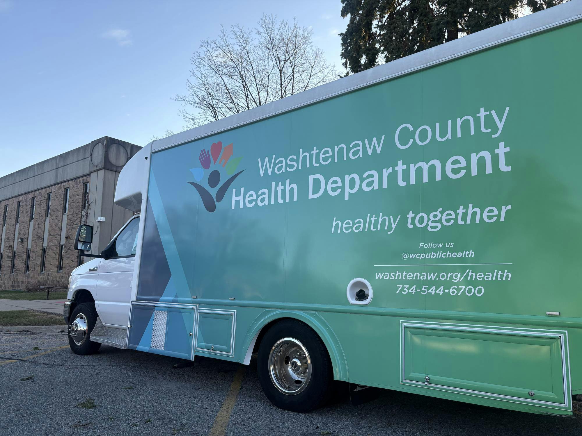 Large commercial van parked along sidewalk. Graphics on the van read "Washtenaw County Health Department, healthy together."