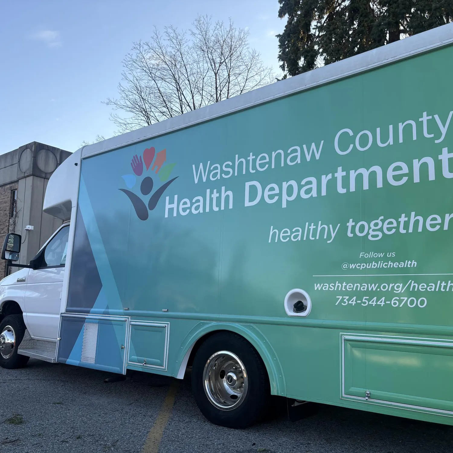 Large commercial van parked along sidewalk. Graphics on the van read "Washtenaw County Health Department, healthy together."