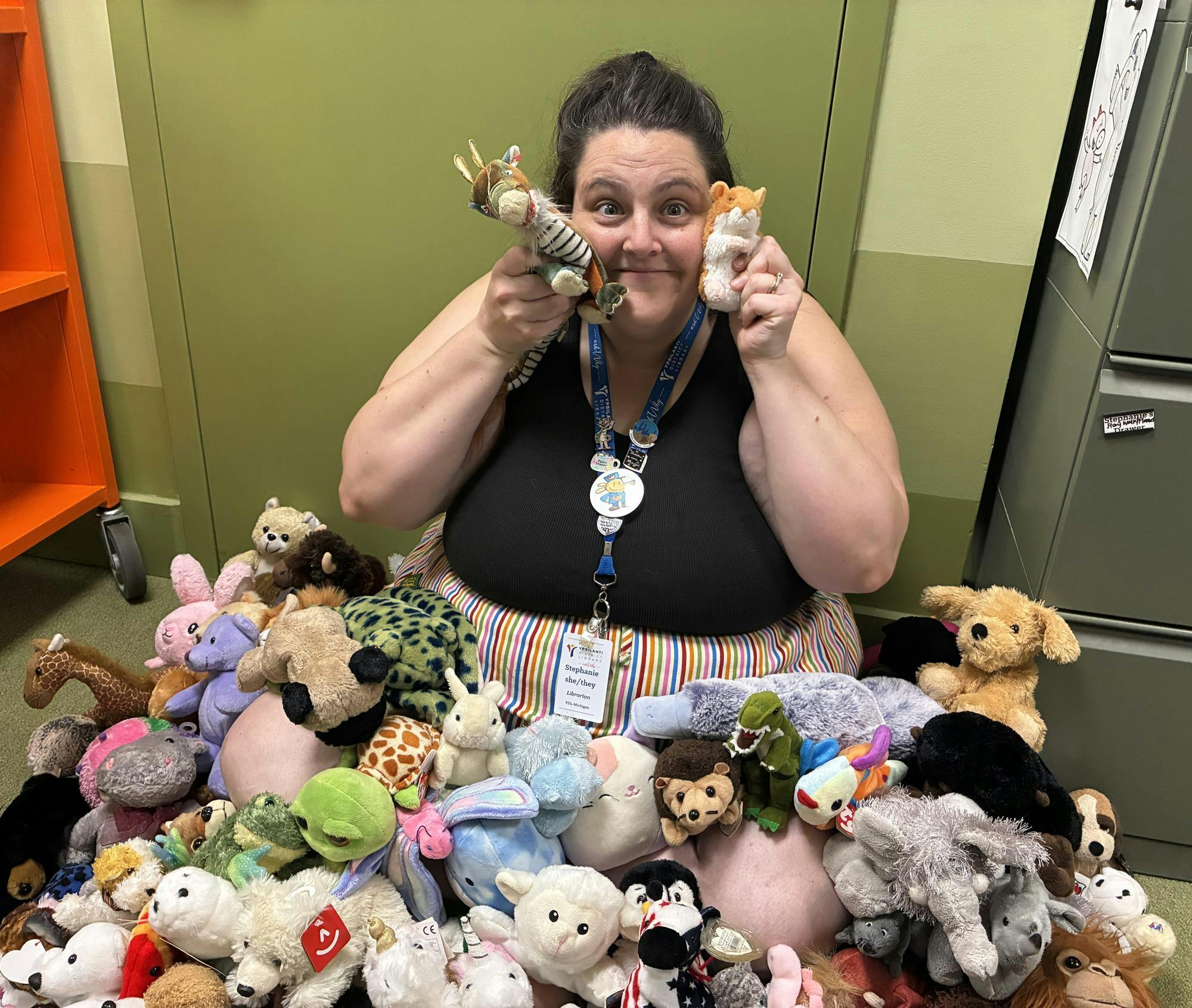 Stephanie Pocsi-Morrison sits surrounded by various stuffed animals of different types and colors.