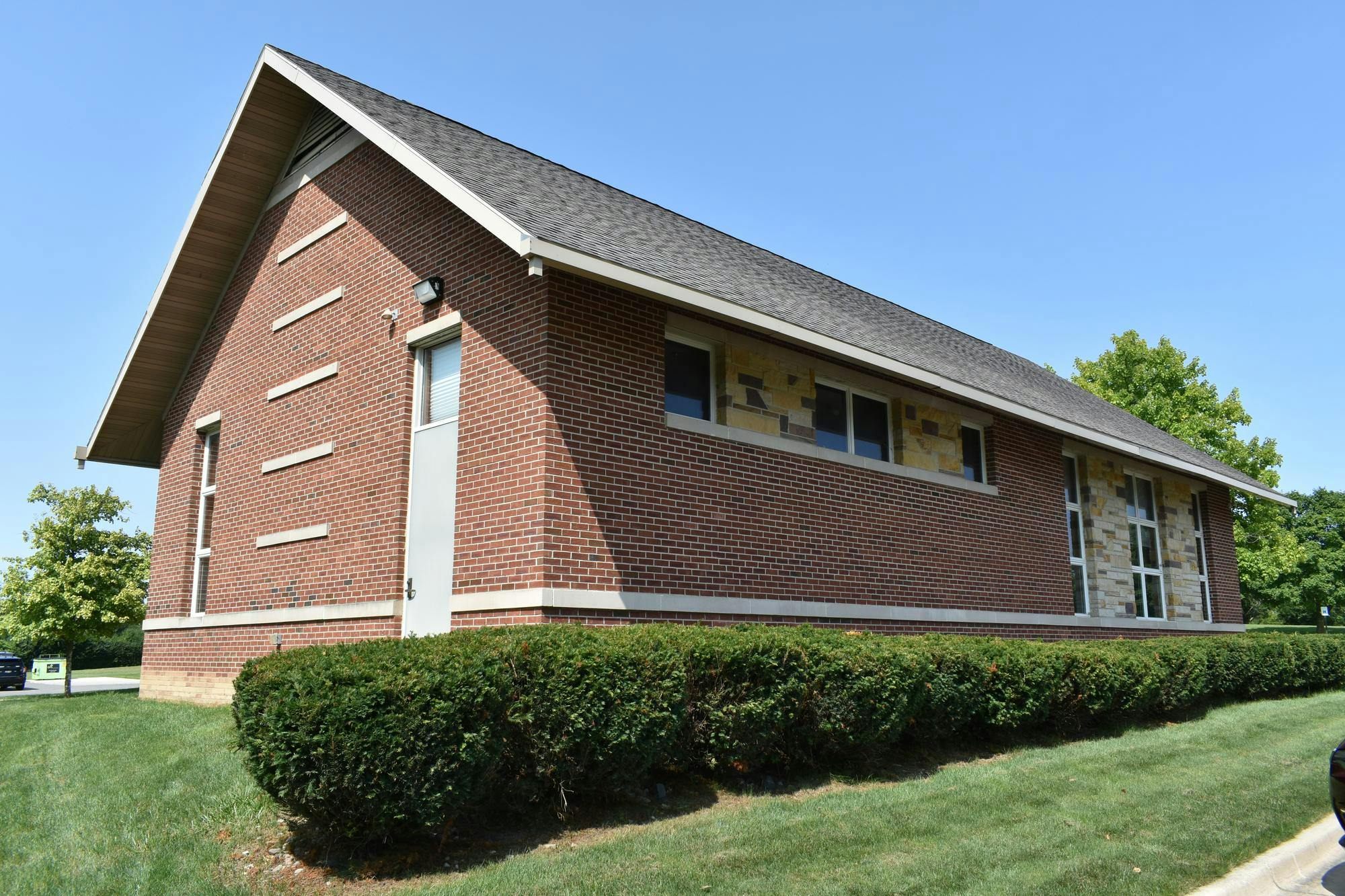 Brown brick building with trimmed hedges surrounding it, viewed from the corner. 