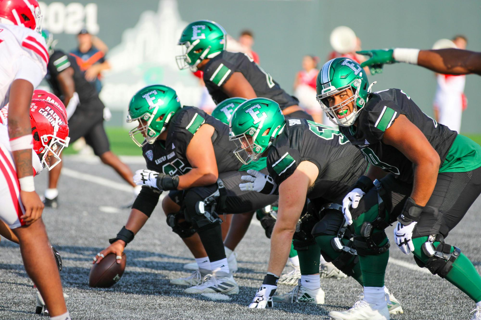 The EMU offensive line prepares to snap the ball against the Louisiana Ragin' Cajuns. An EMU player looks towards the camera.