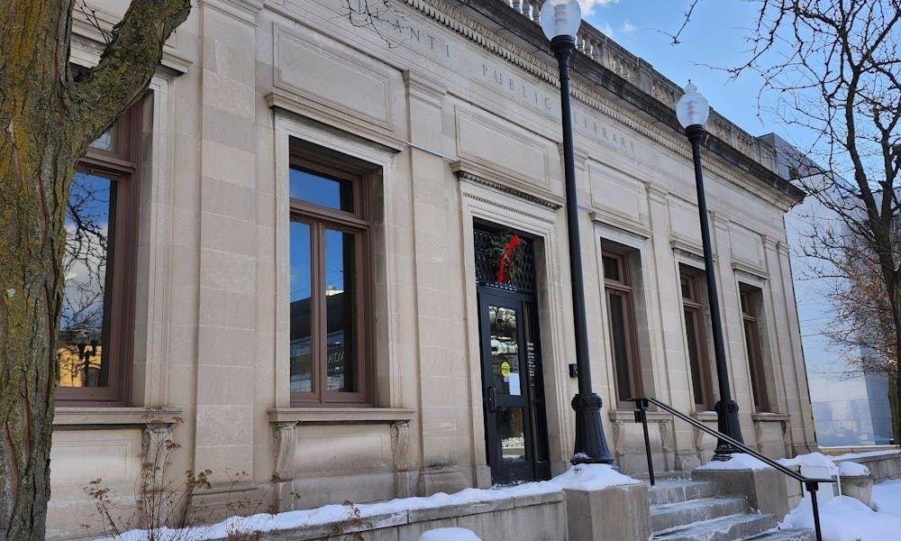 A large, cream-colored building with several stairs leading up to a front glass door. Carved into the front of the building near the top are the words "Ypsilanti Public Library," written in all capital letters.