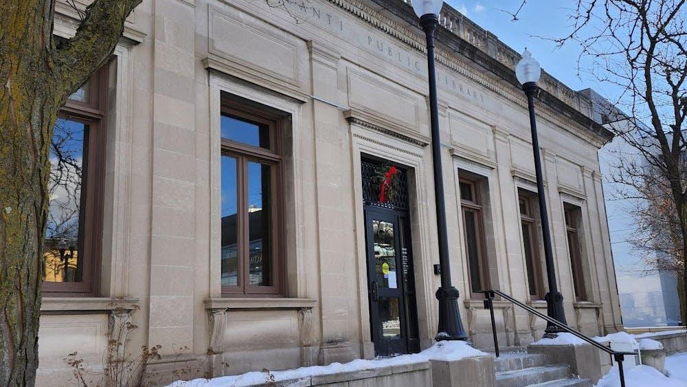 A large, cream-colored building with several stairs leading up to a front glass door. Carved into the front of the building near the top are the words "Ypsilanti Public Library," written in all capital letters.