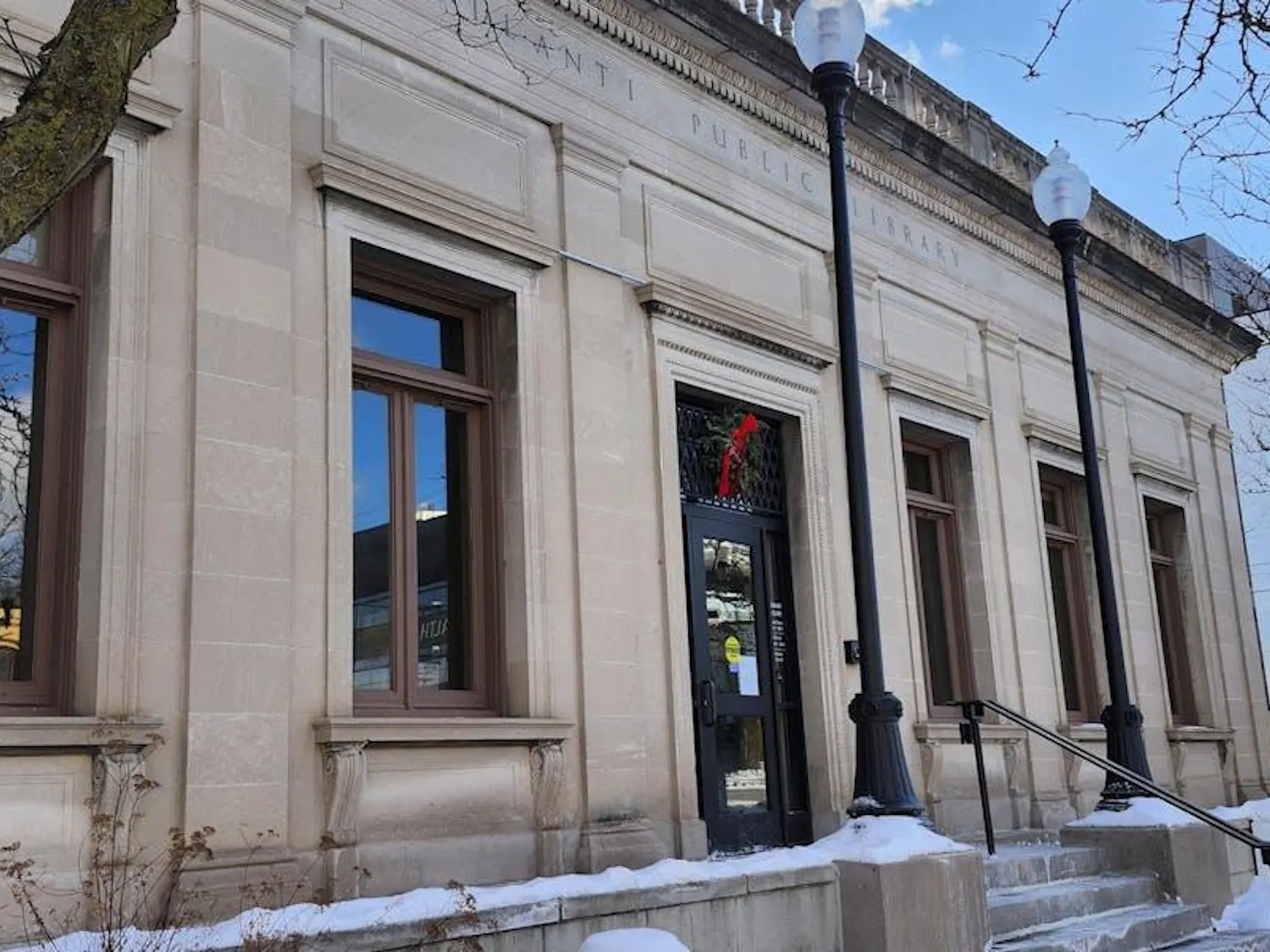 A large, cream-colored building with several stairs leading up to a front glass door. Carved into the front of the building near the top are the words "Ypsilanti Public Library," written in all capital letters.