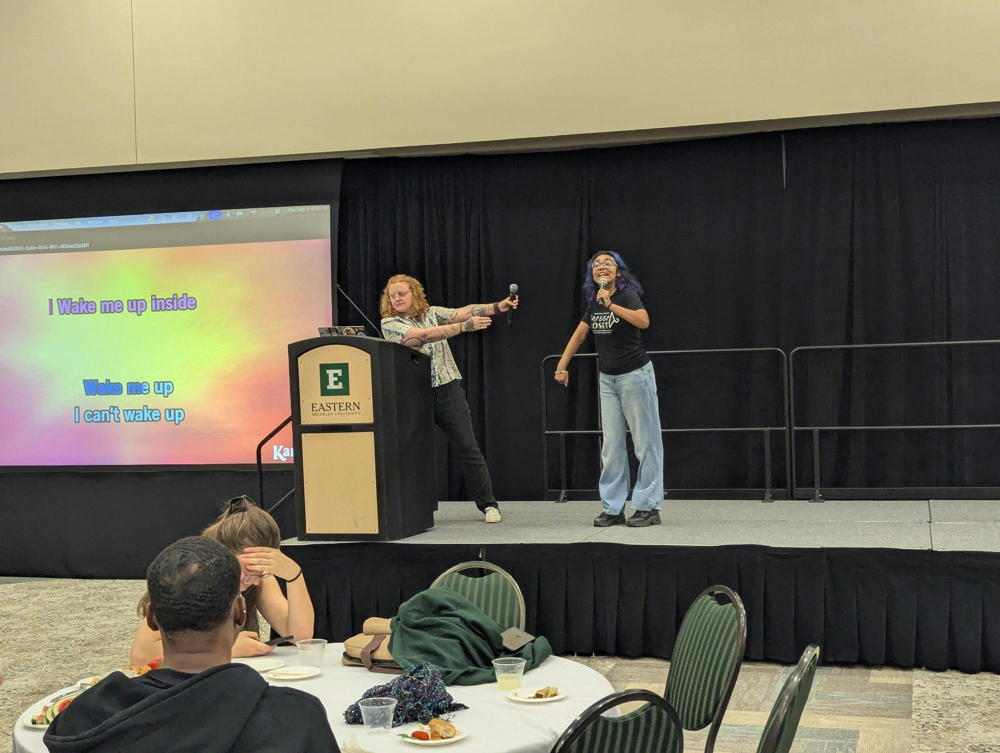 Two individuals holding microphones sing karaoke.