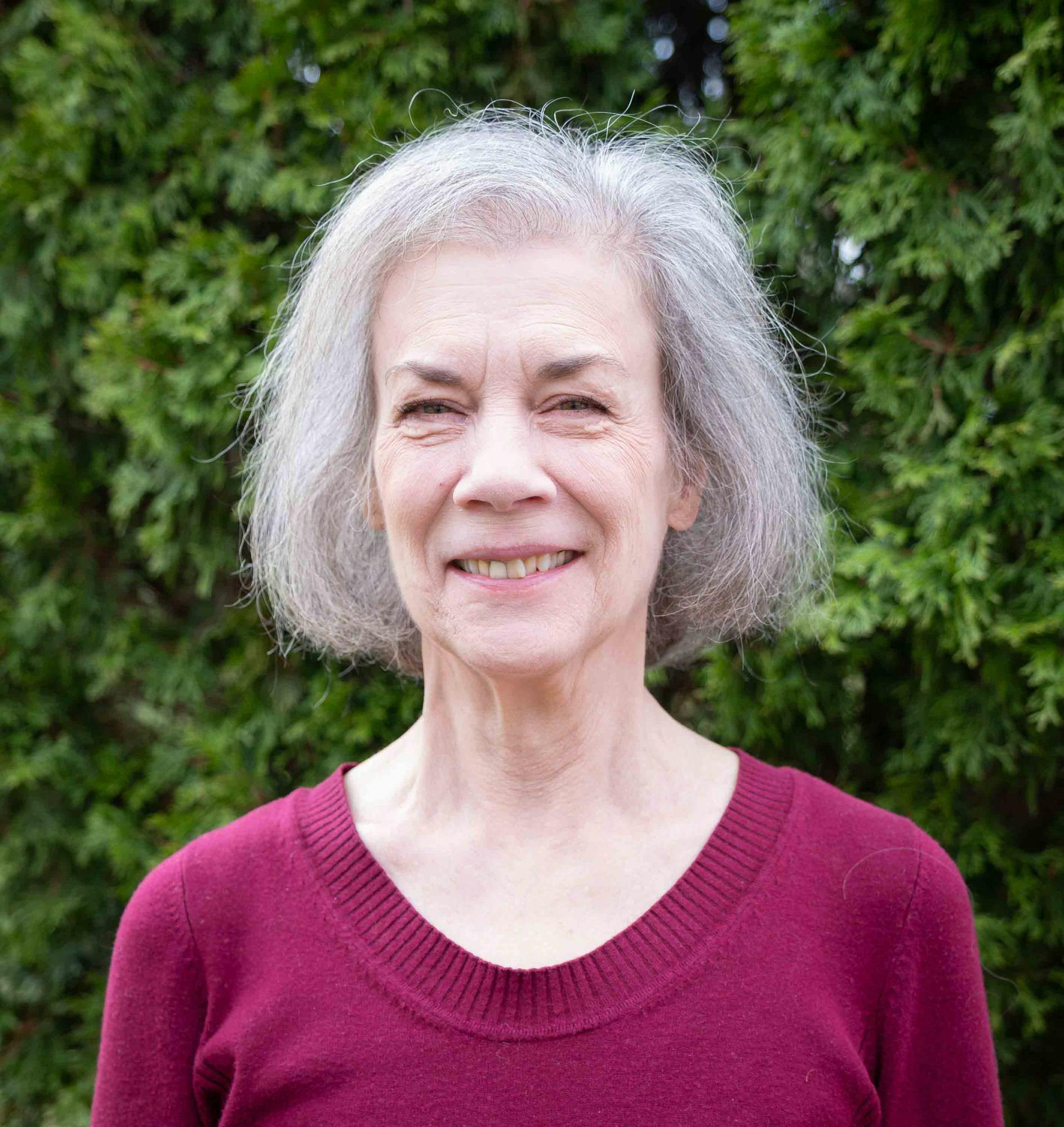 Sally Wright Day smiles outdoors in front of green foliage.