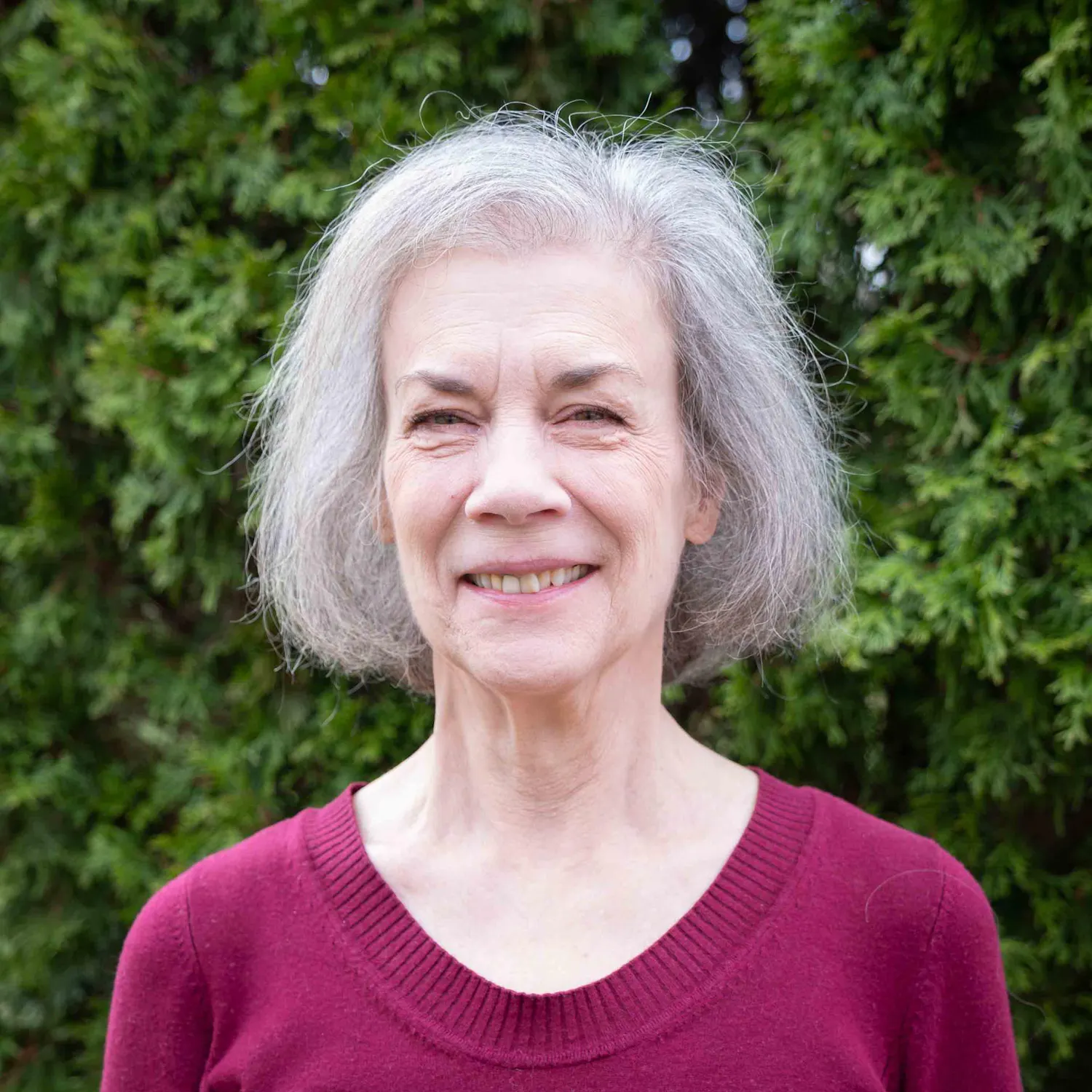 Sally Wright Day smiles outdoors in front of green foliage.