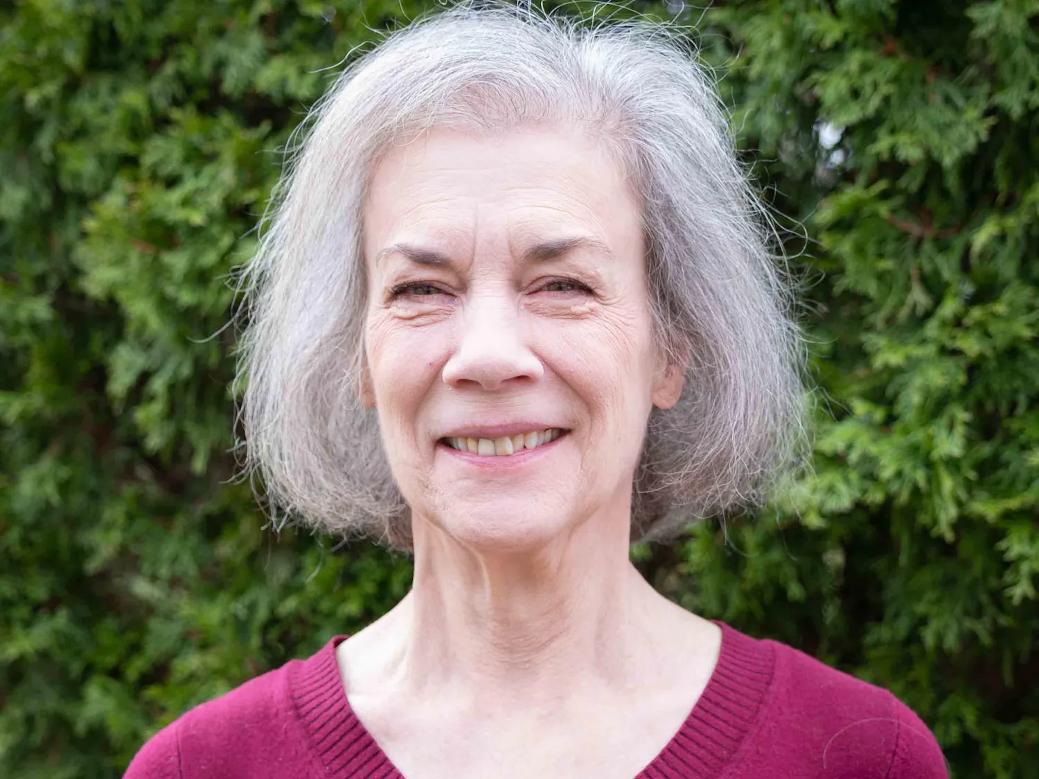 Sally Wright Day smiles outdoors in front of green foliage.